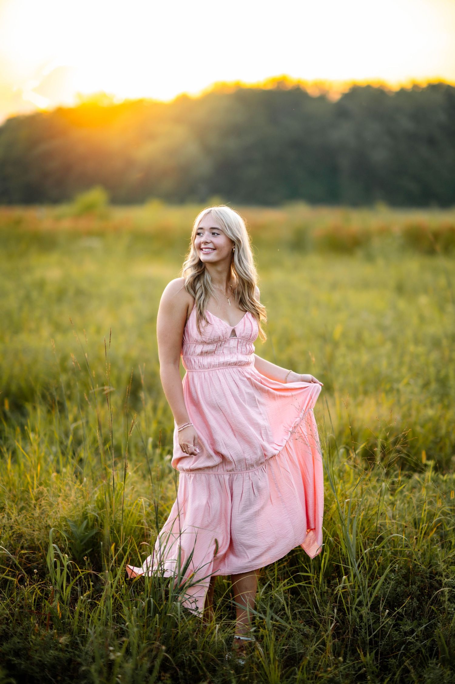 Dreamy sunset photoshoot in pink dress among tall grass in golden field.