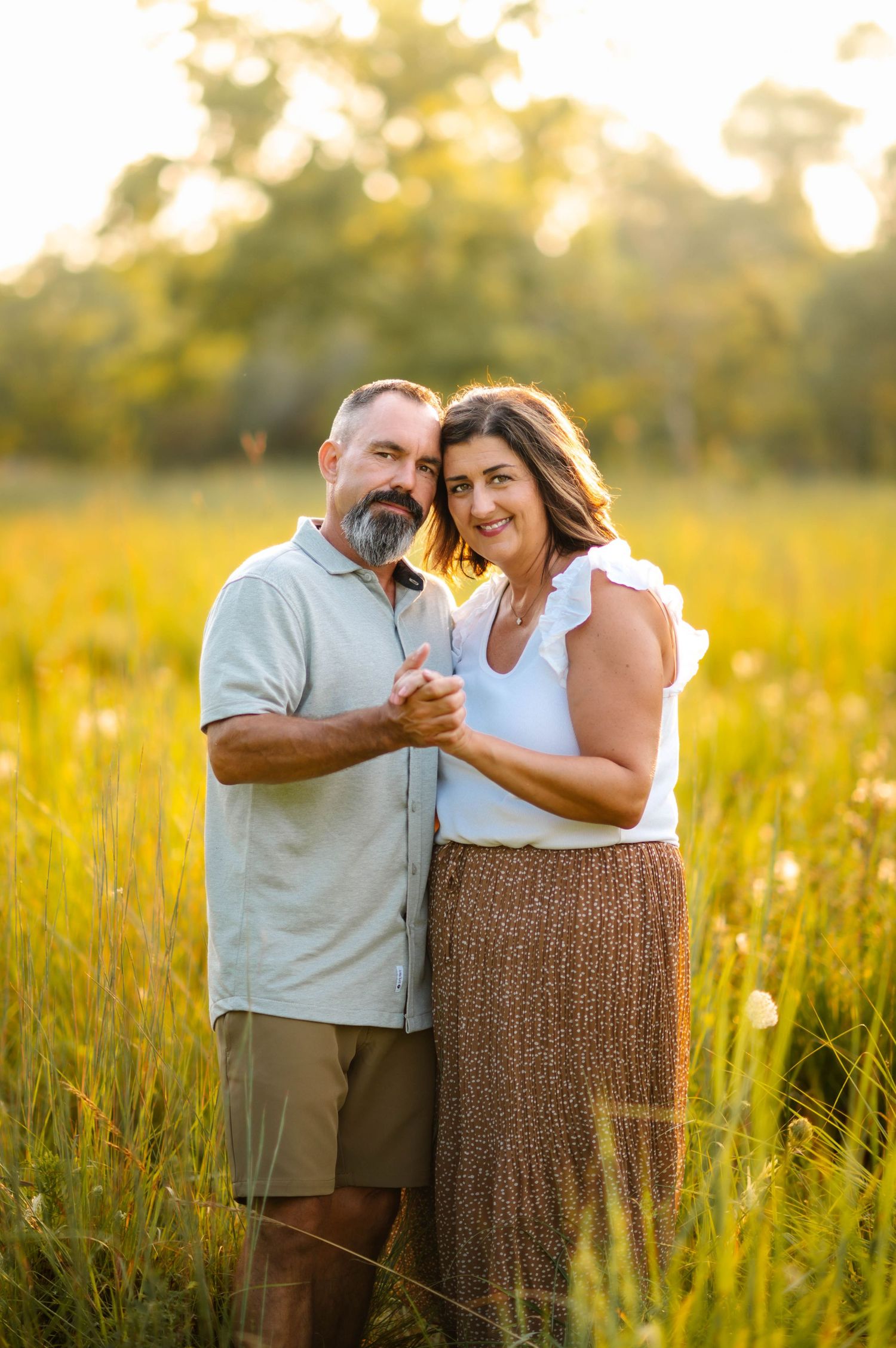 A couple shares a joyful moment while standing in a sunlit meadow with tall grass.