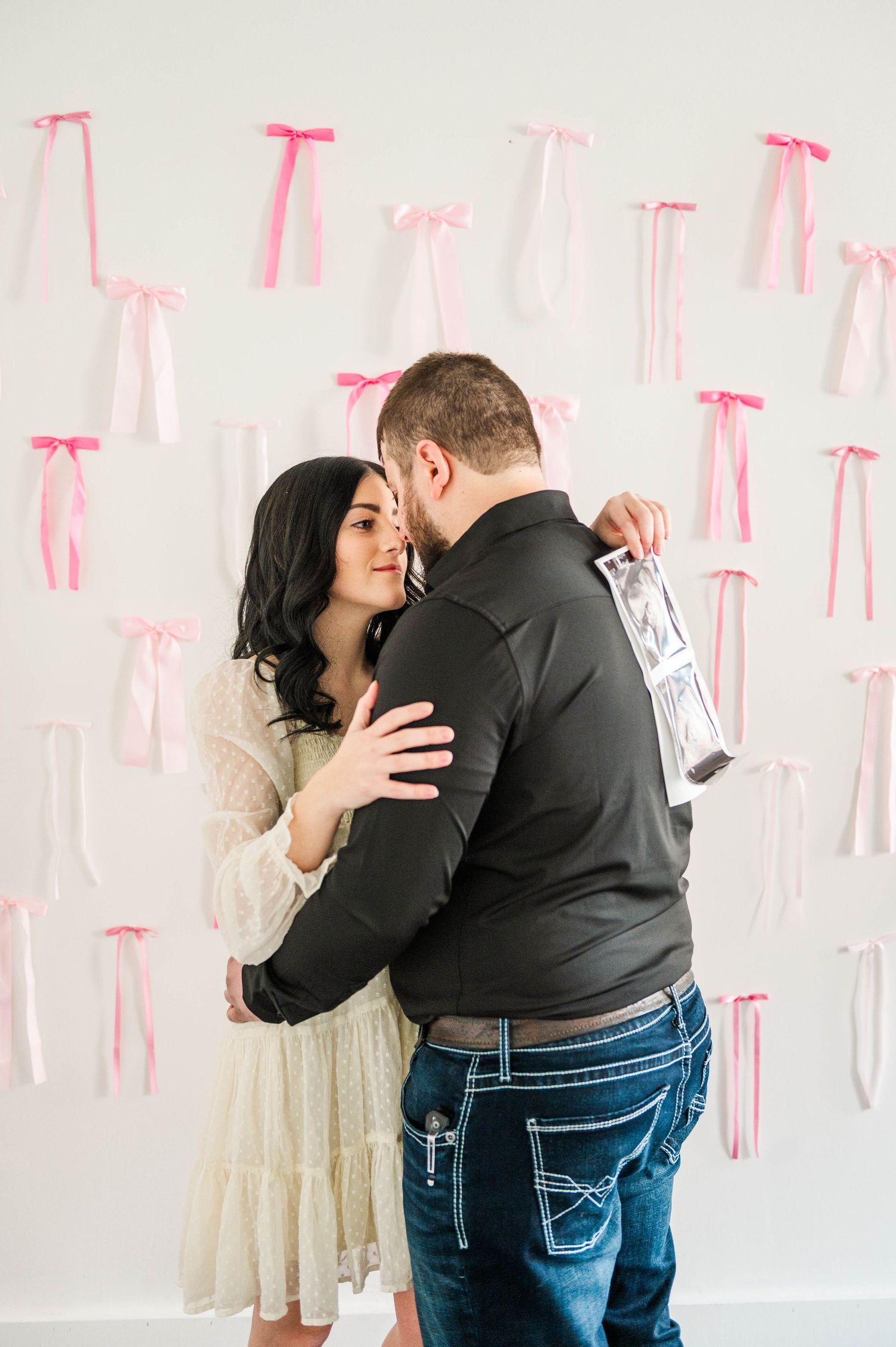 A couple shares an intimate moment while holding sonogram photos against a decorated wall.