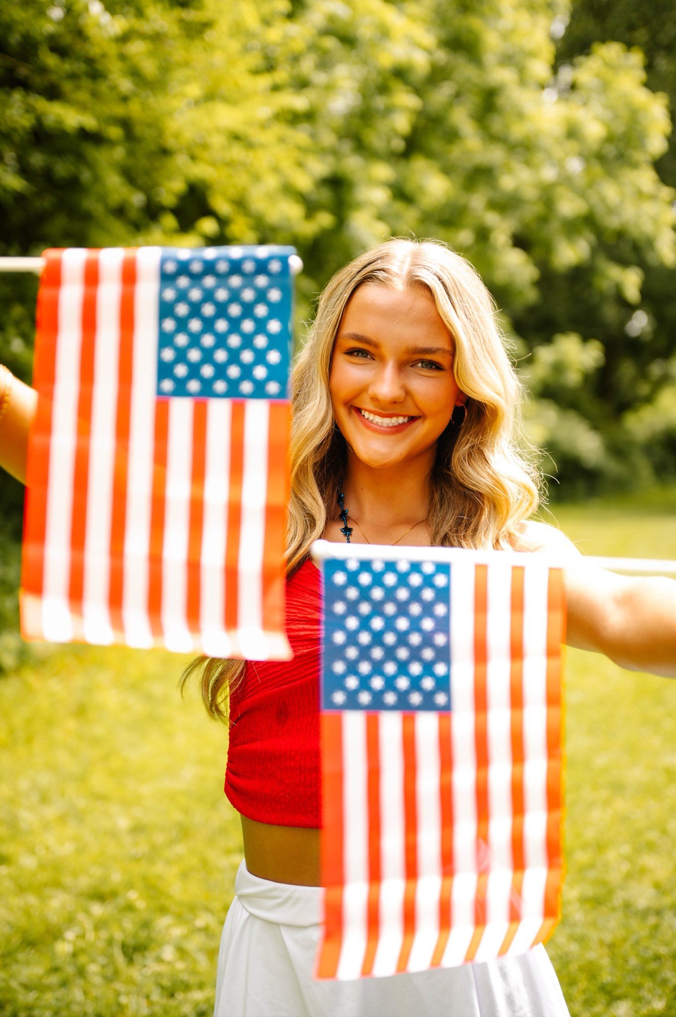 American flags being held up in a sunny outdoor setting with trees in the background.