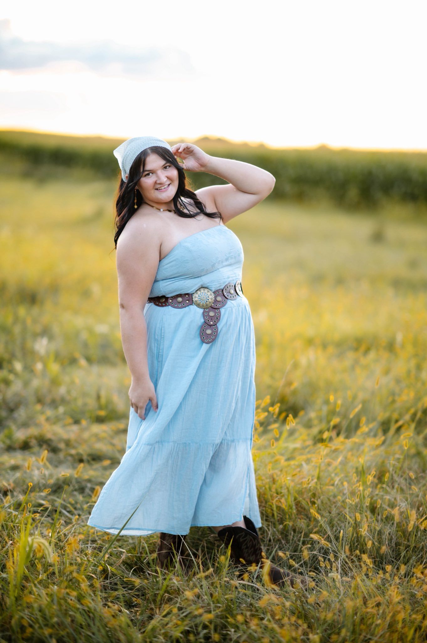 Person in flowing blue dress poses in sunlit meadow with wildflowers.