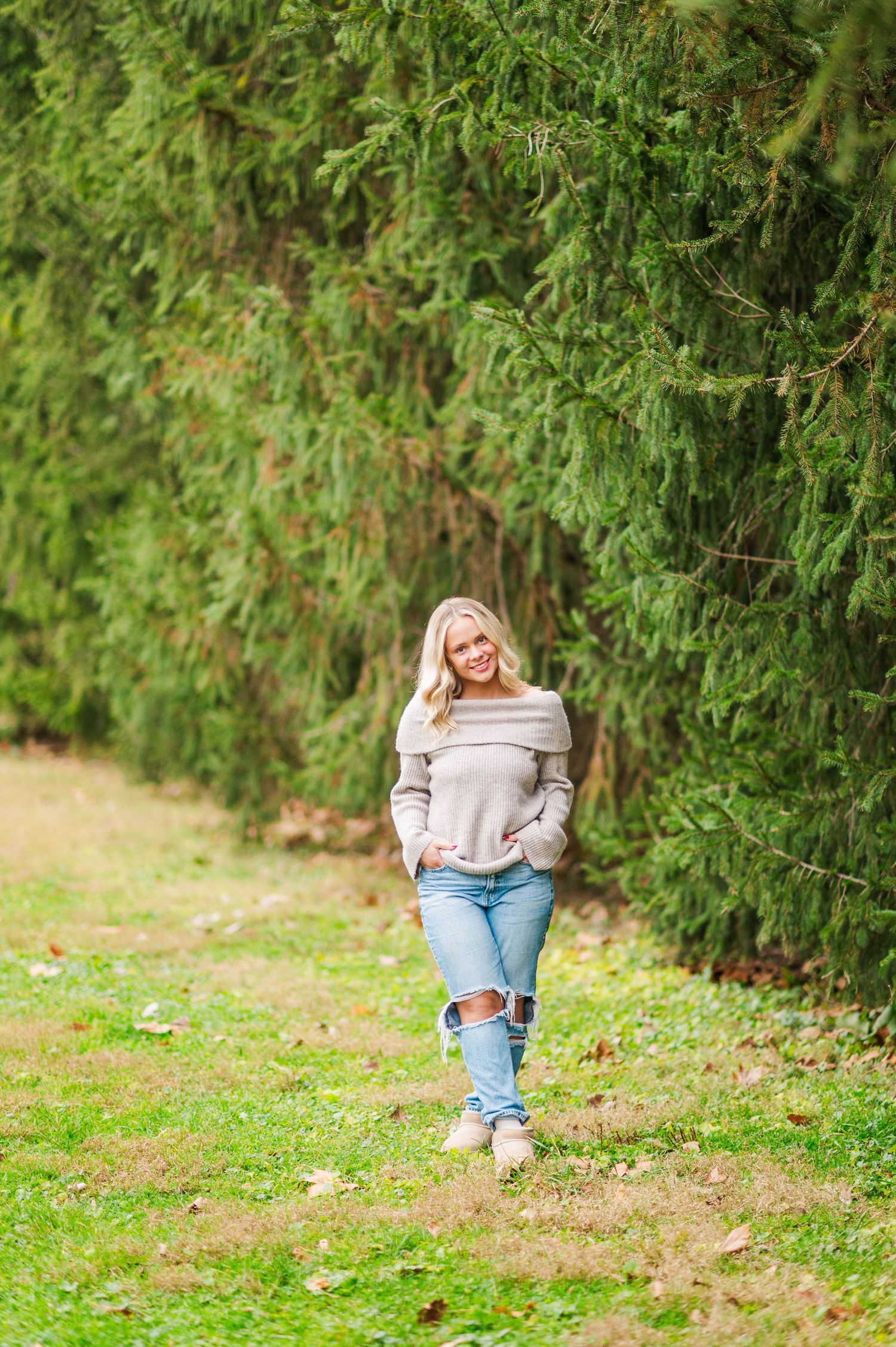 A person sits in casual attire against a backdrop of evergreen trees in a natural outdoor setting.