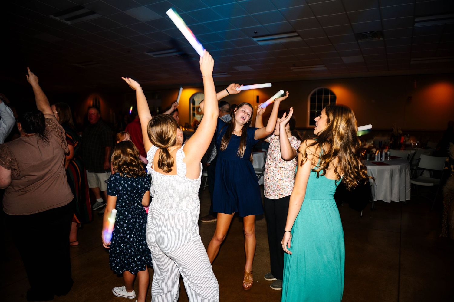 Wedding reception dance floor filled with guests dancing under dark lighting.
