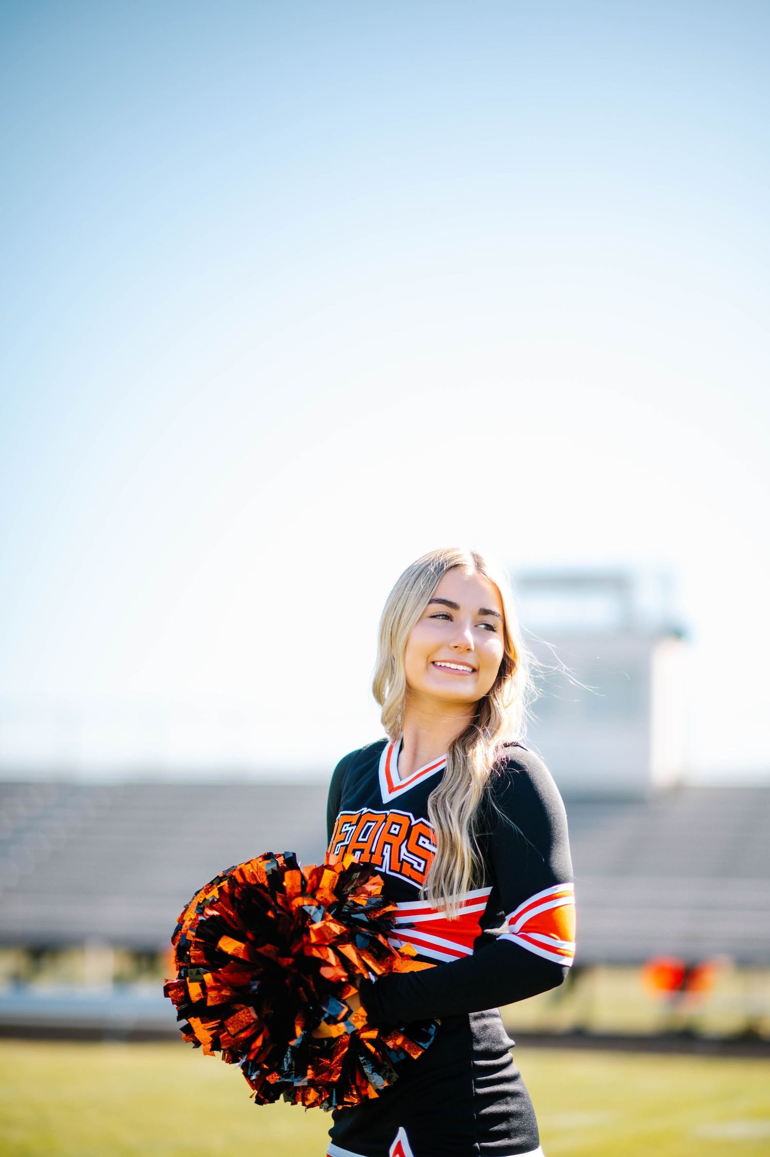 Cheerleader in black and orange uniform smiles while performing outdoors.