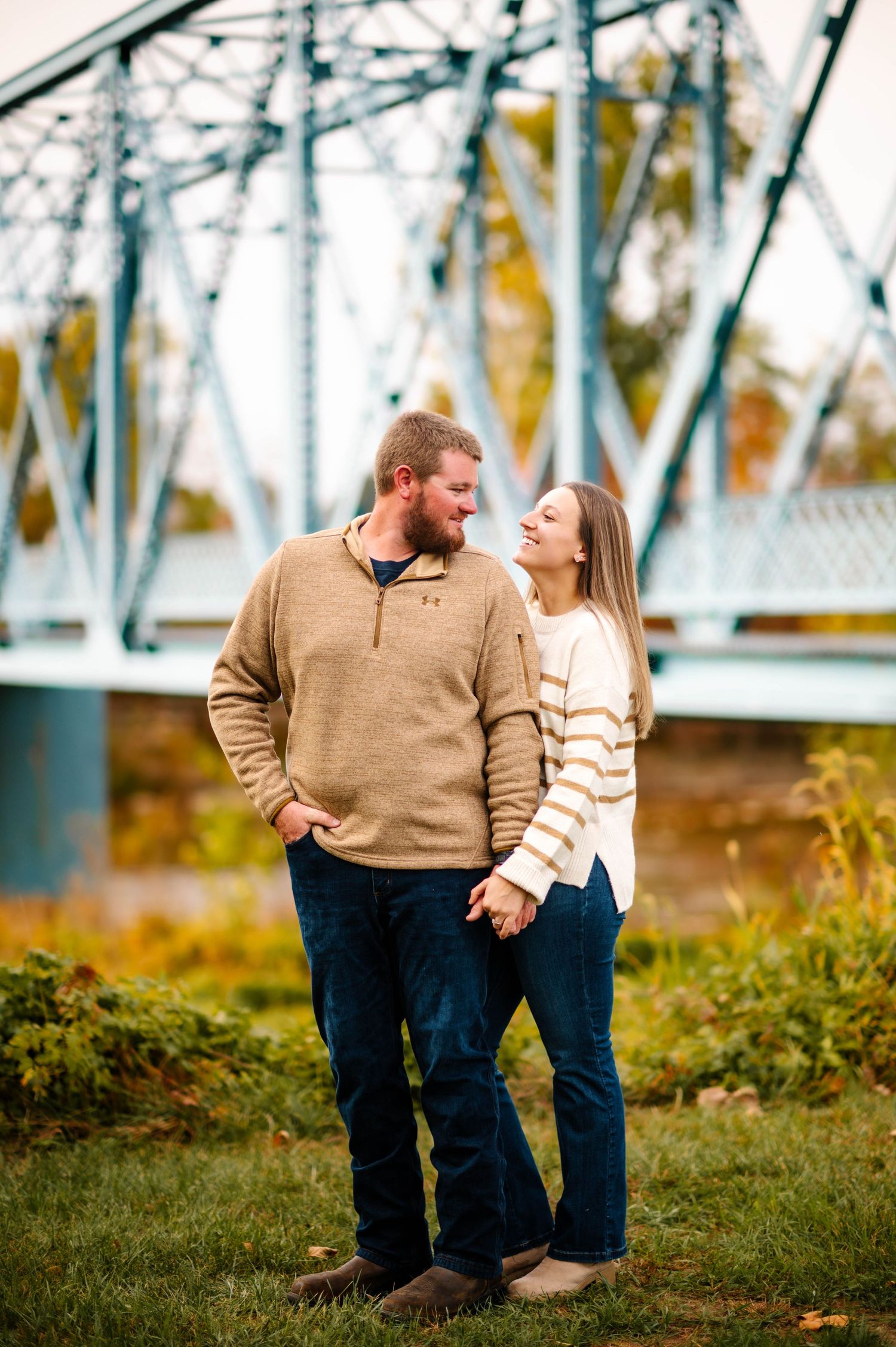 Romantic couple in matching sweaters share intimate moment by metal bridge structure during fall season.