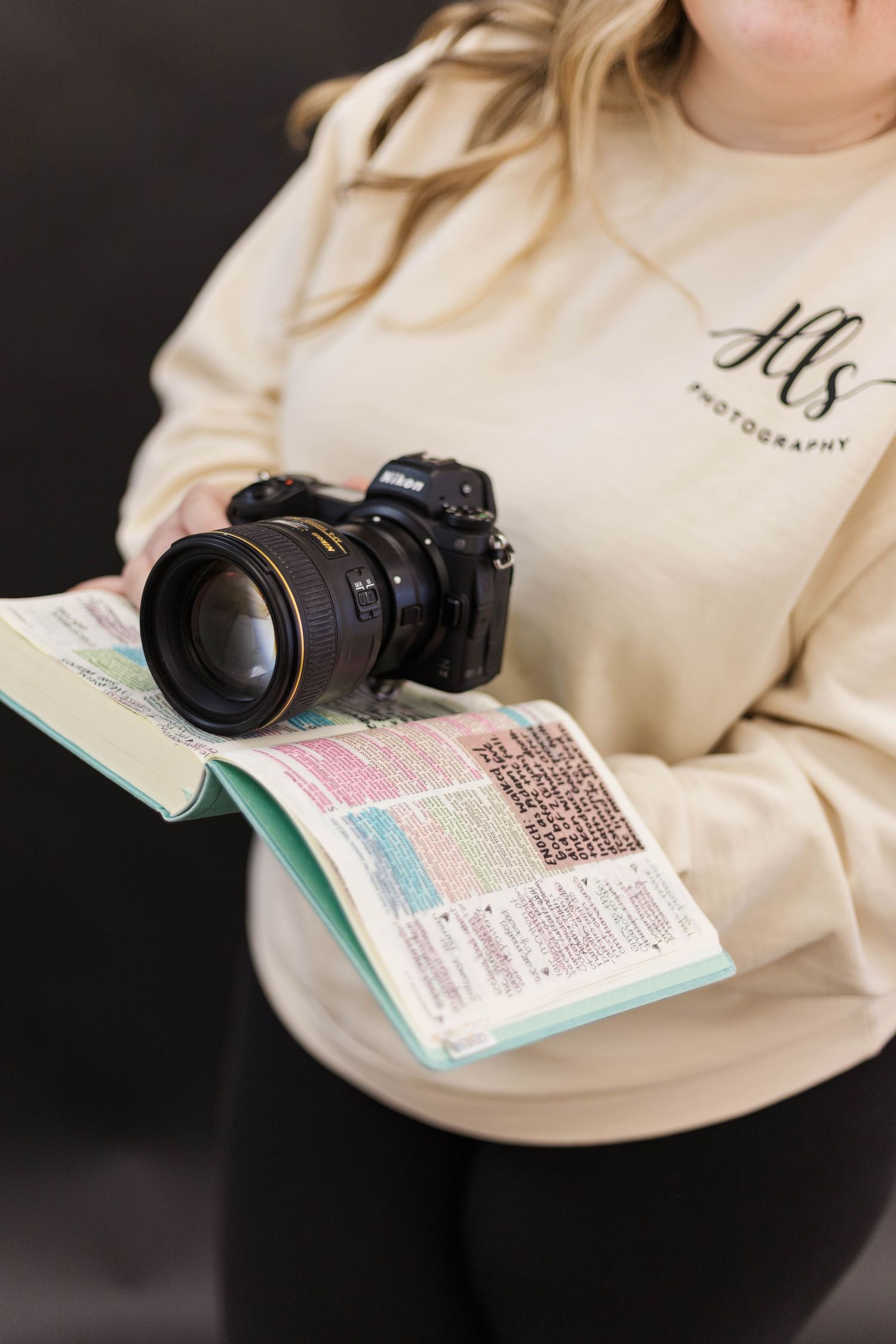 Camera lens and open book displayed on cream-colored surface.