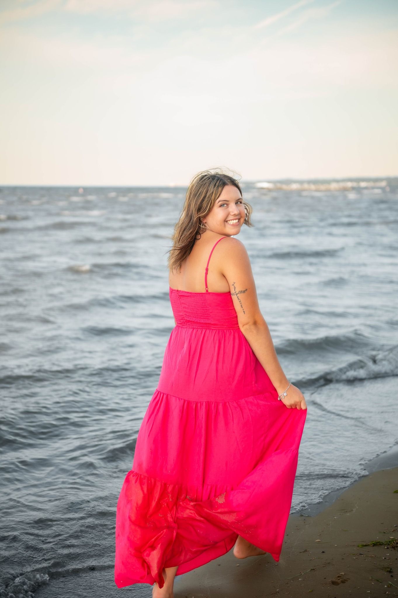 Person in flowing red dress twirling on beach at sunset.