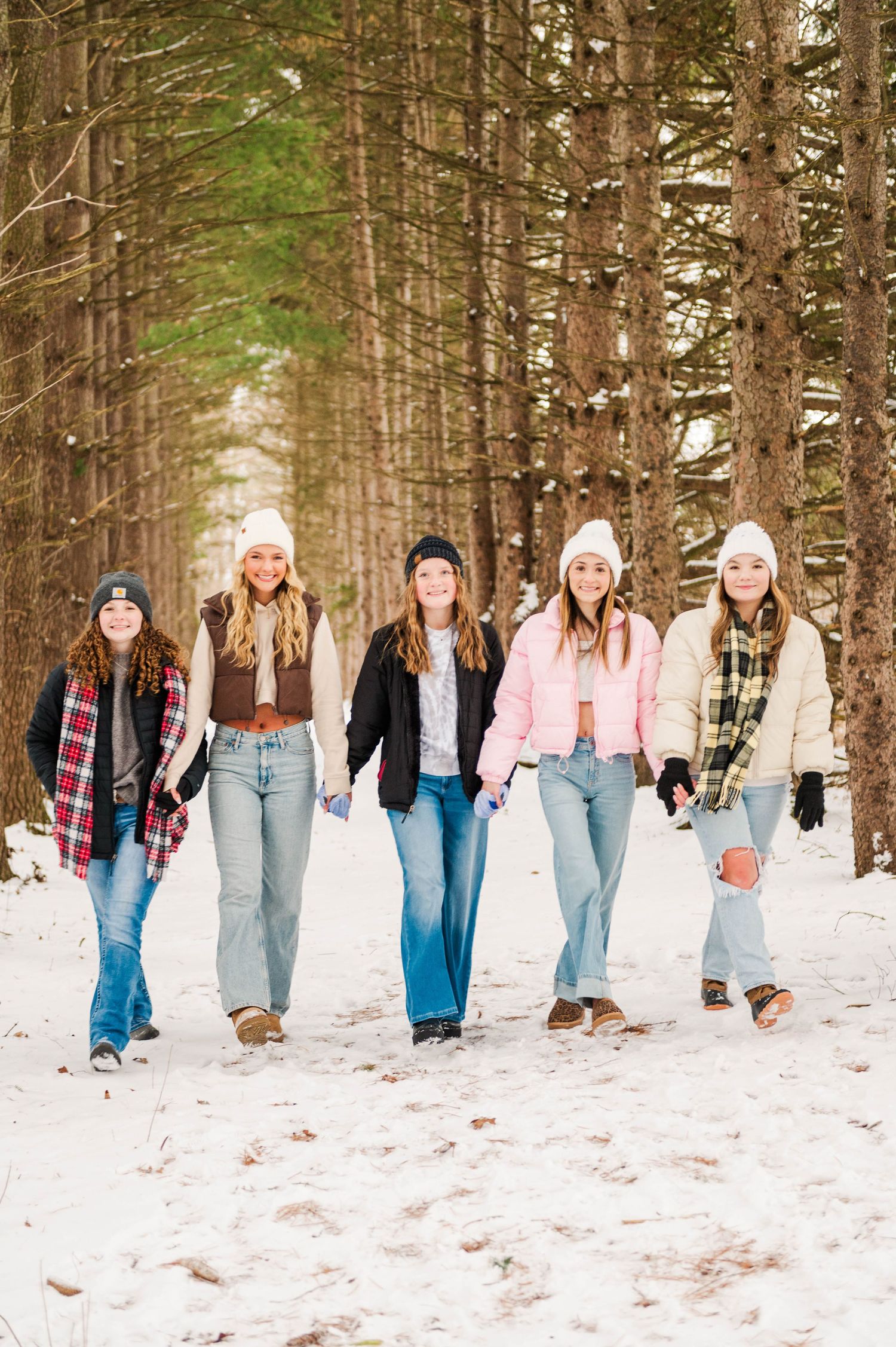 Group walking through snowy forest path wearing coordinated winter casual clothing.