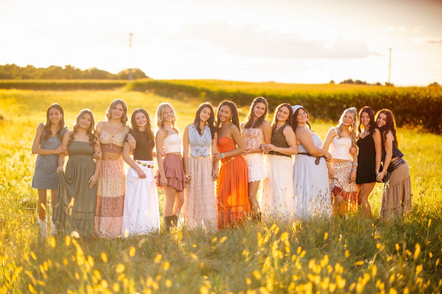 Line of people in light dresses standing in golden field at sunset.