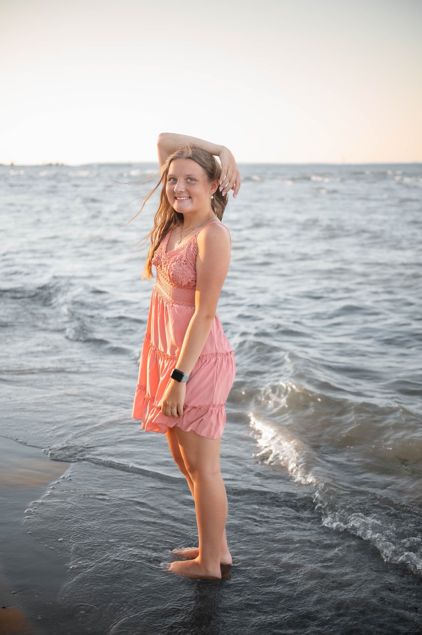 Person in coral dress playing in ocean waves during sunset photoshoot.