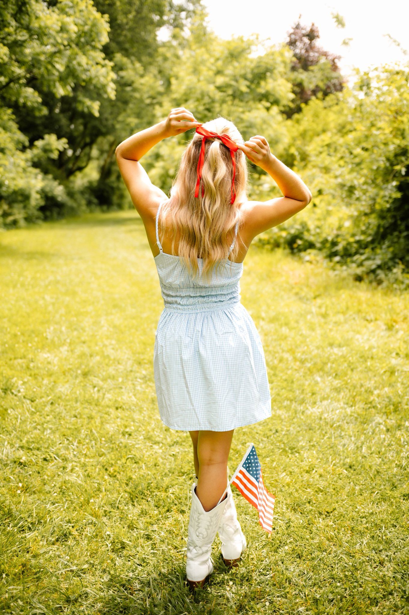Person in light dress twirls with American flag in sunny field.