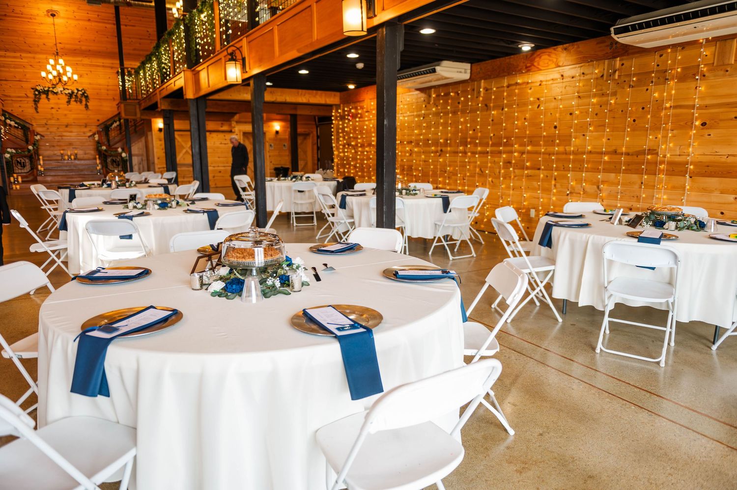 Wedding reception venue with white tablecloths, navy blue accents, and string light decorations.