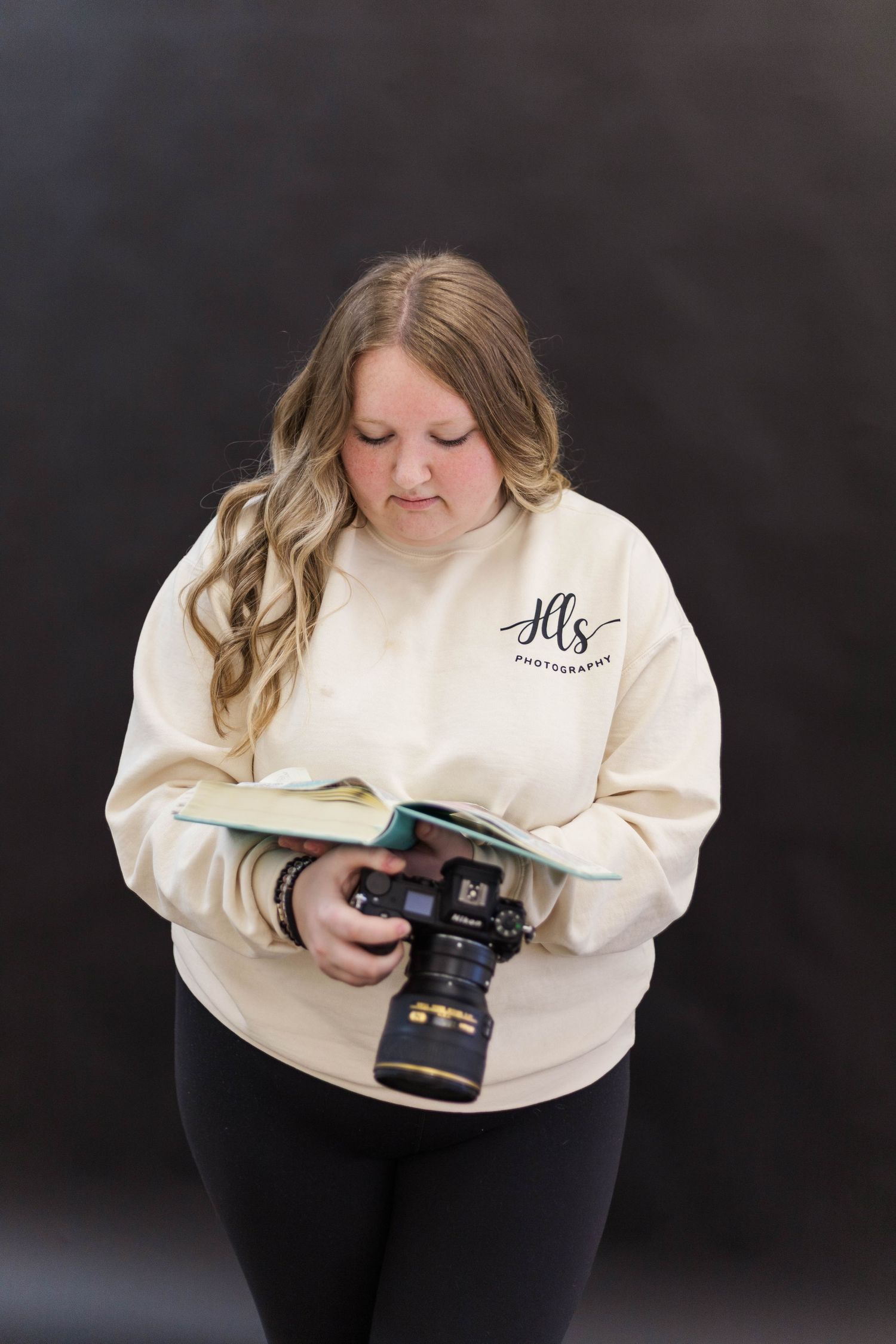 Photographer in cream sweatshirt examines camera while sitting.