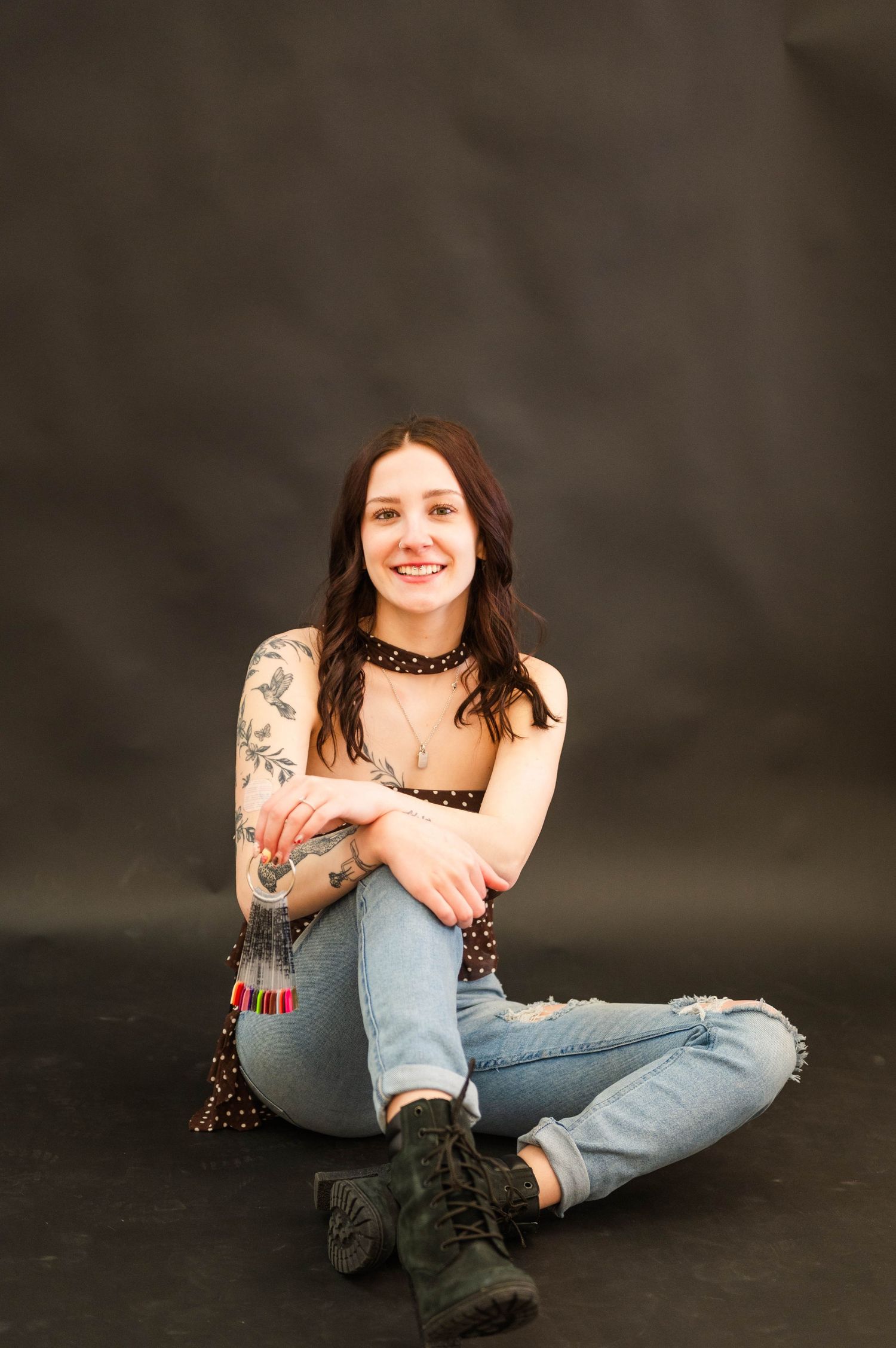 A person in casual wear and boots sits casually against a dark studio backdrop.