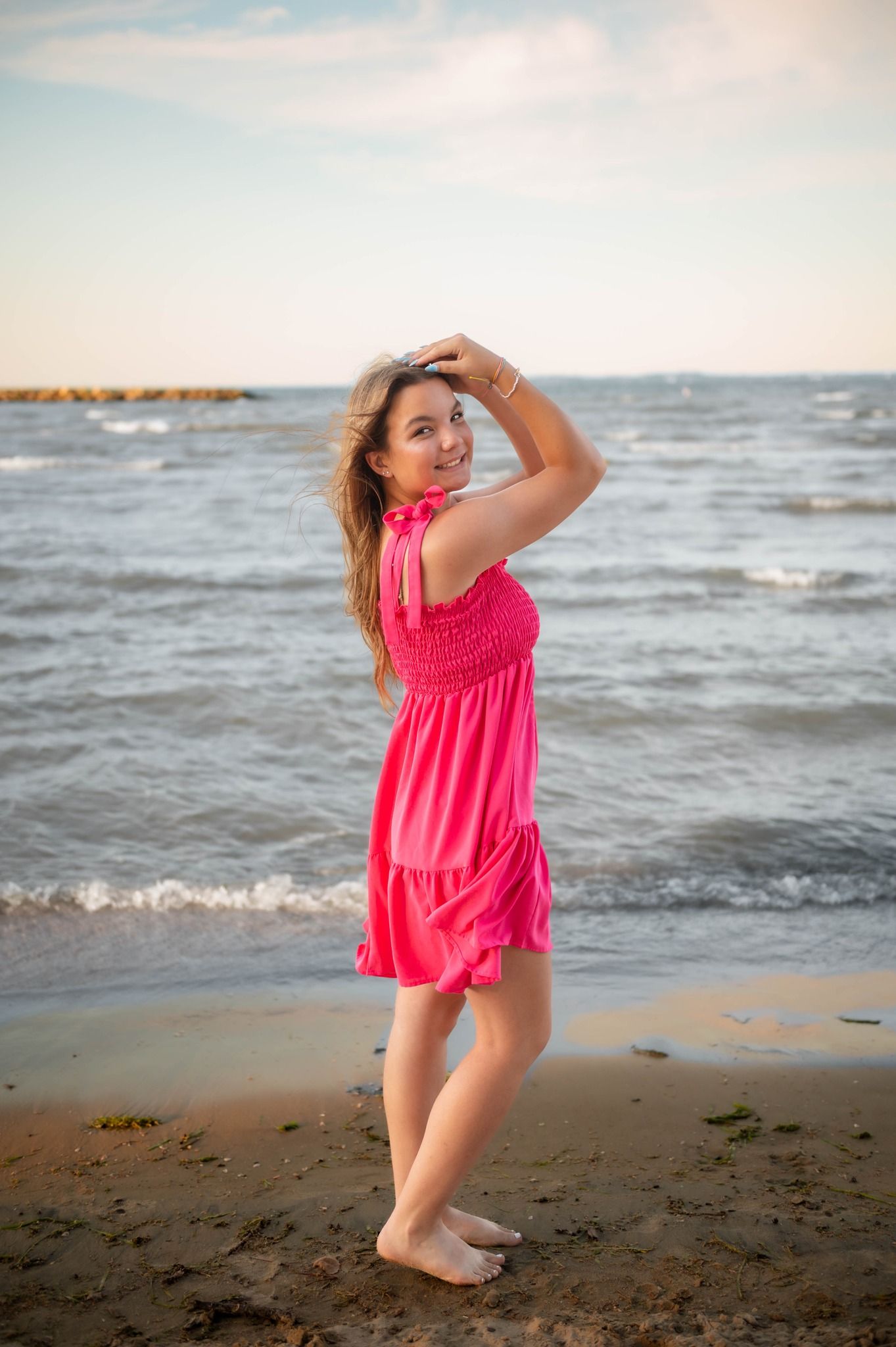 Person in bright pink swimsuit posing playfully on beach near ocean waves.