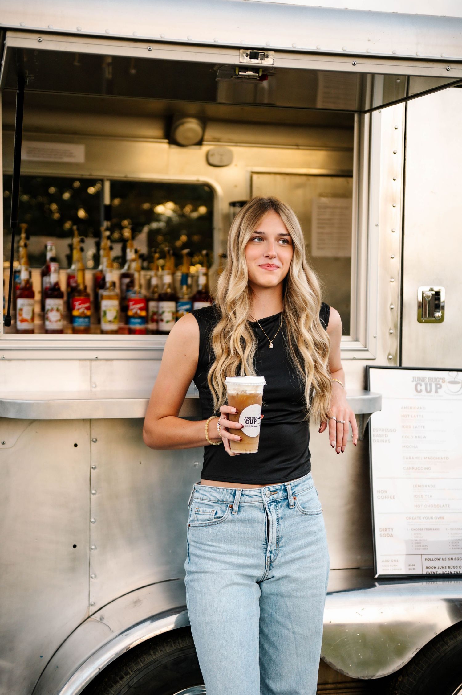 Woman in casual attire serving beverages from white food truck window.