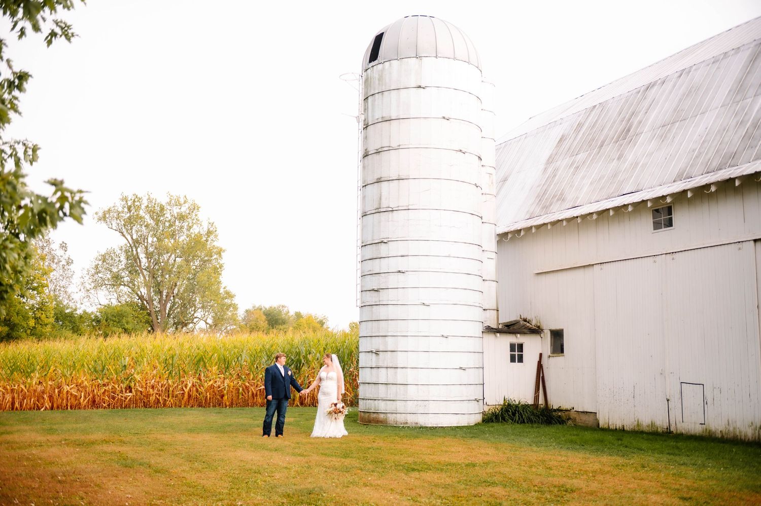 Rural farm setting with white silos and barn provides backdrop for wedding photos.