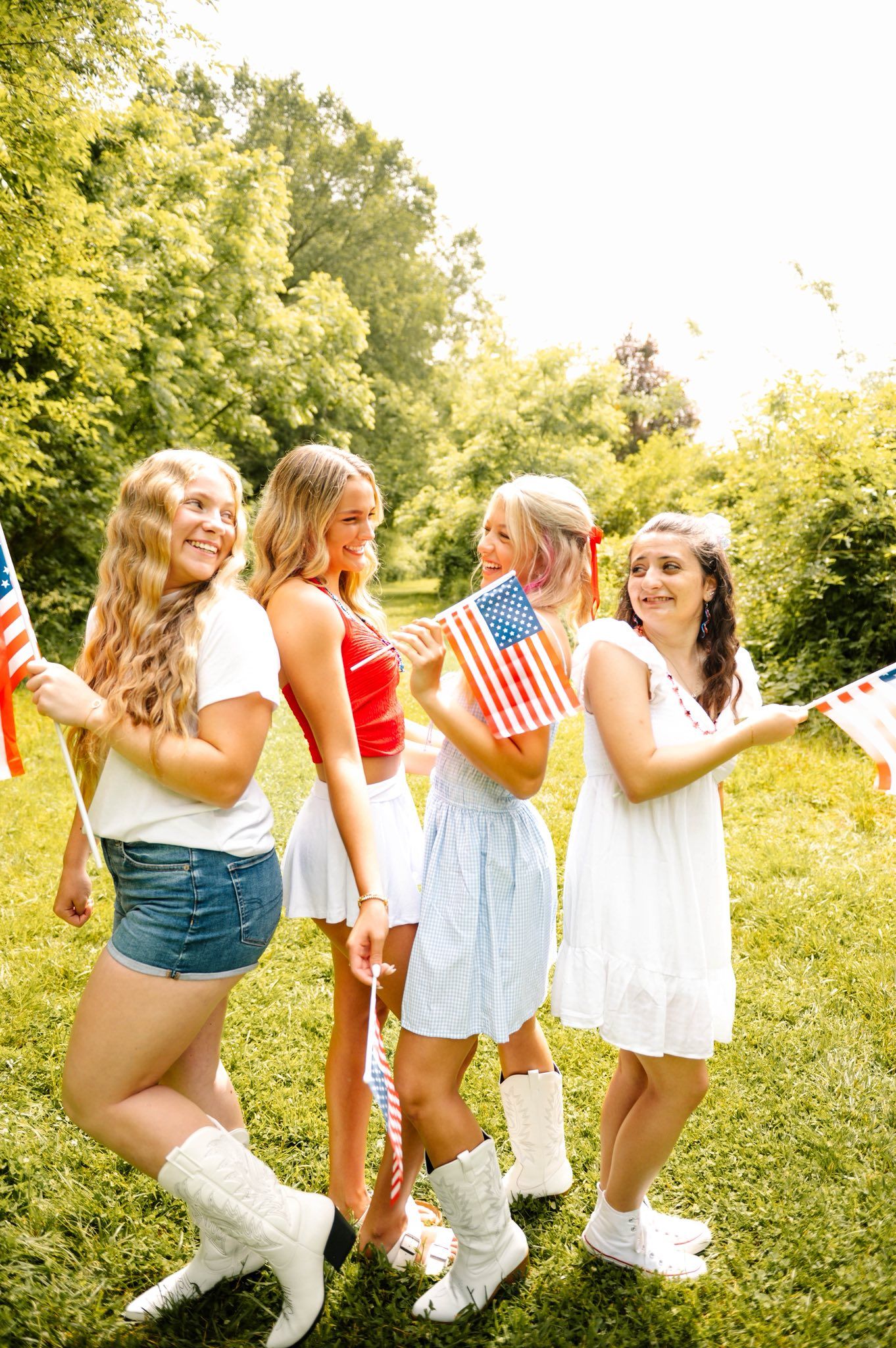 Friends in summer outfits dance together while holding American flags outdoors.