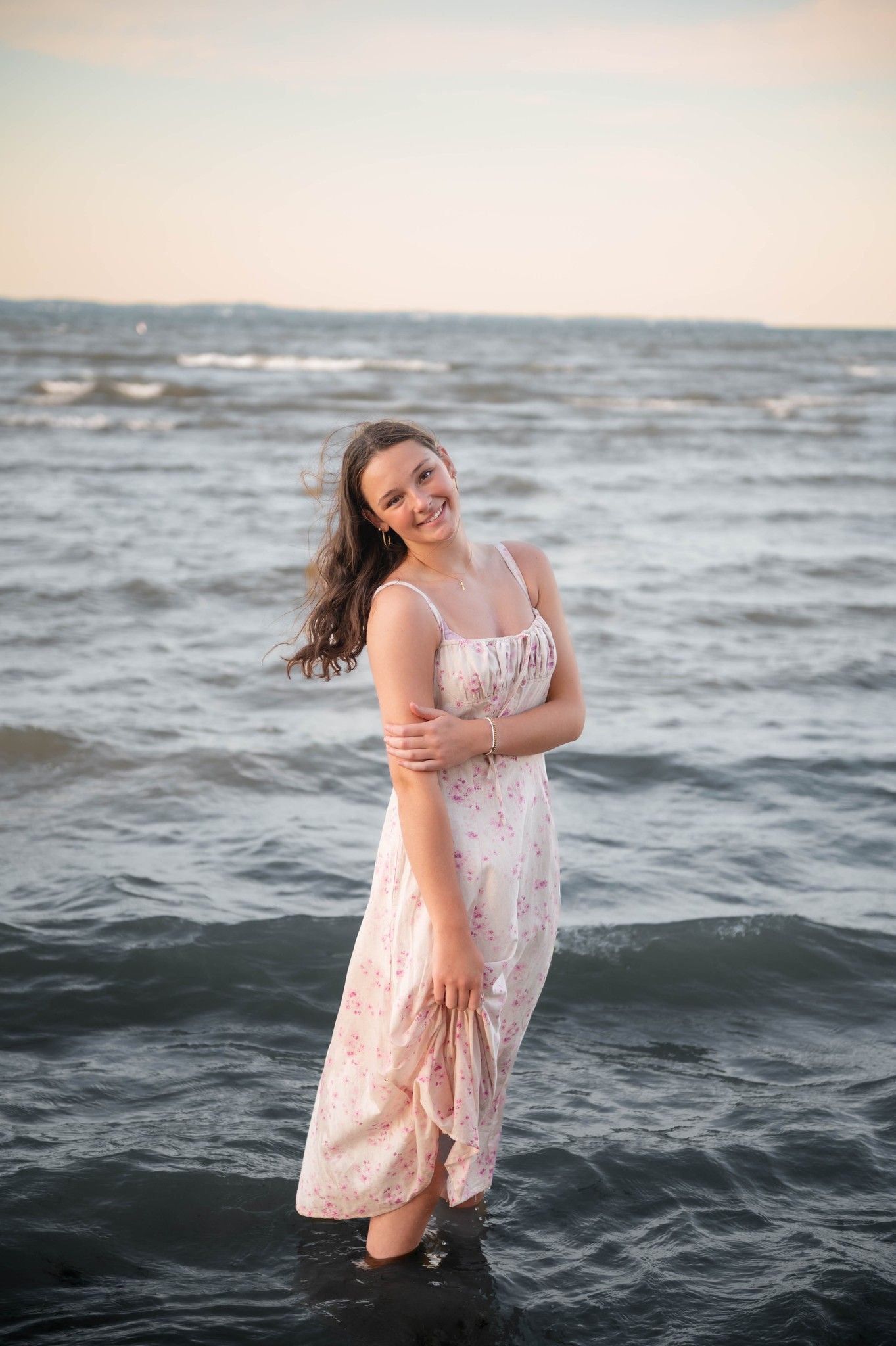 Woman in pink dress laughing and playing in ocean waves at sunset.