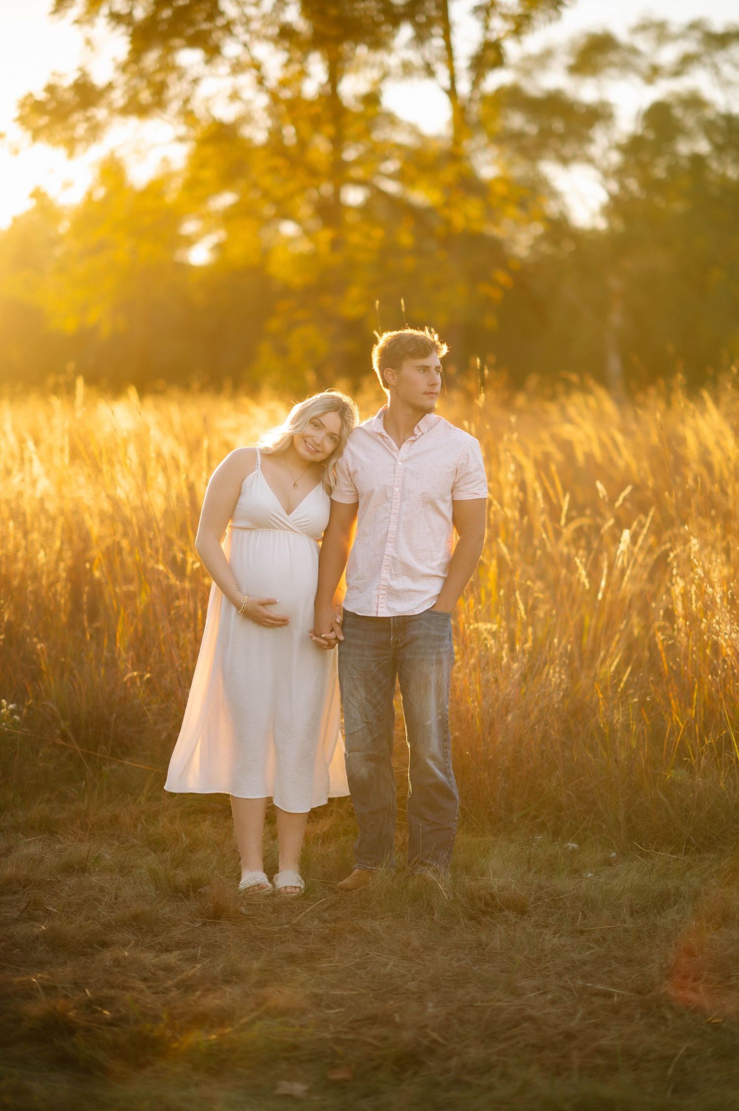 Couple embracing in tall grass during golden hour sunset photoshoot.