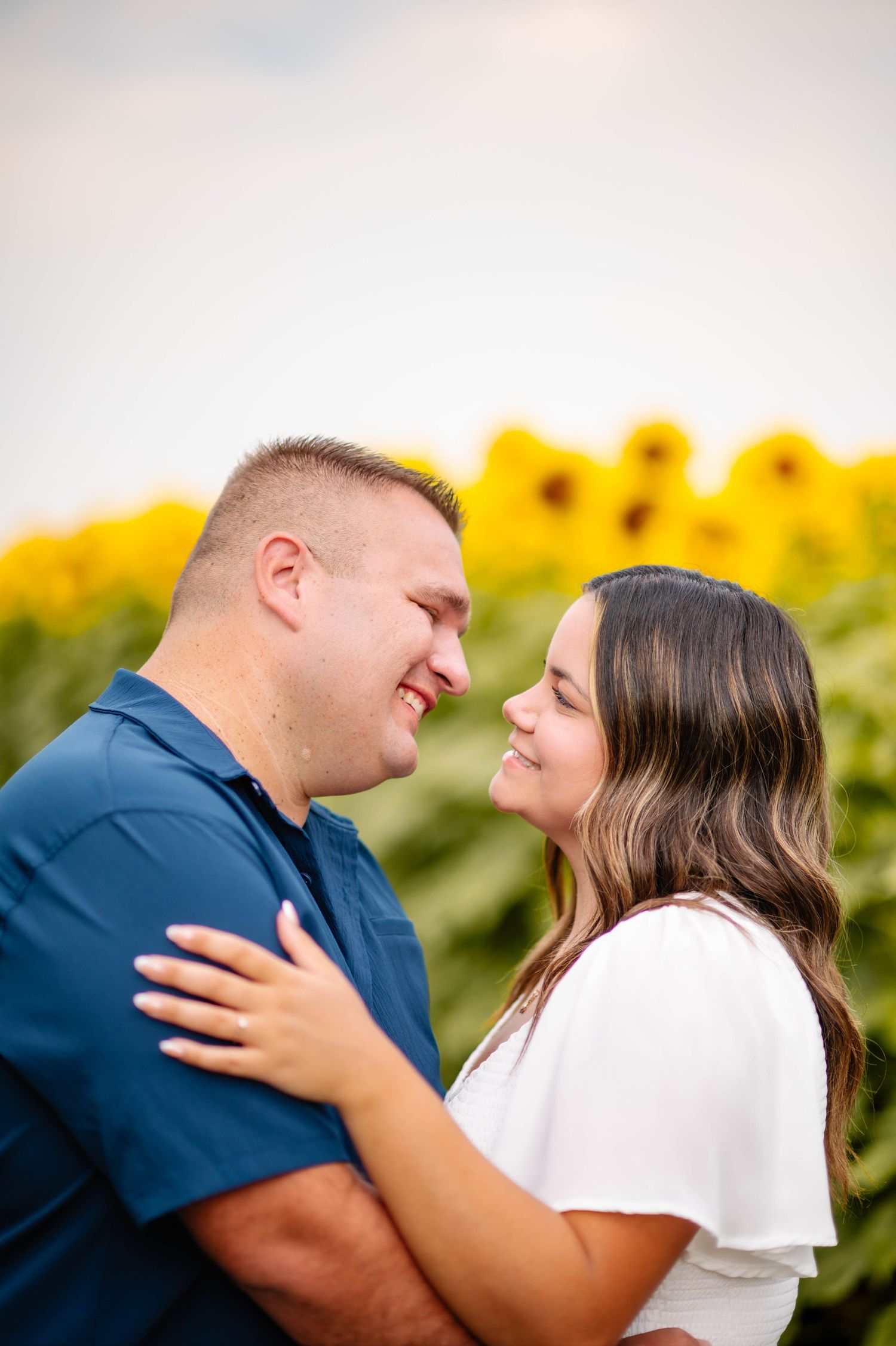 A couple shares an intimate moment together in a sunflower field wearing blue and white outfits.