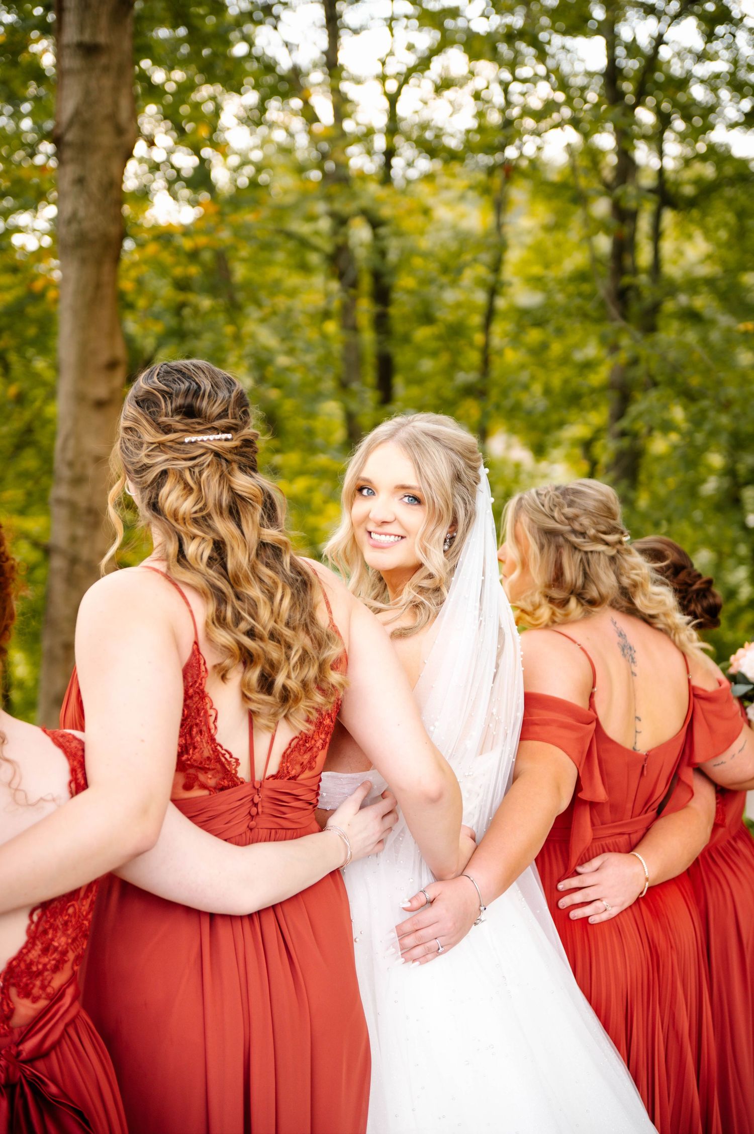 Wedding party wearing red bridesmaid dresses and white gown pose together in a forest setting.