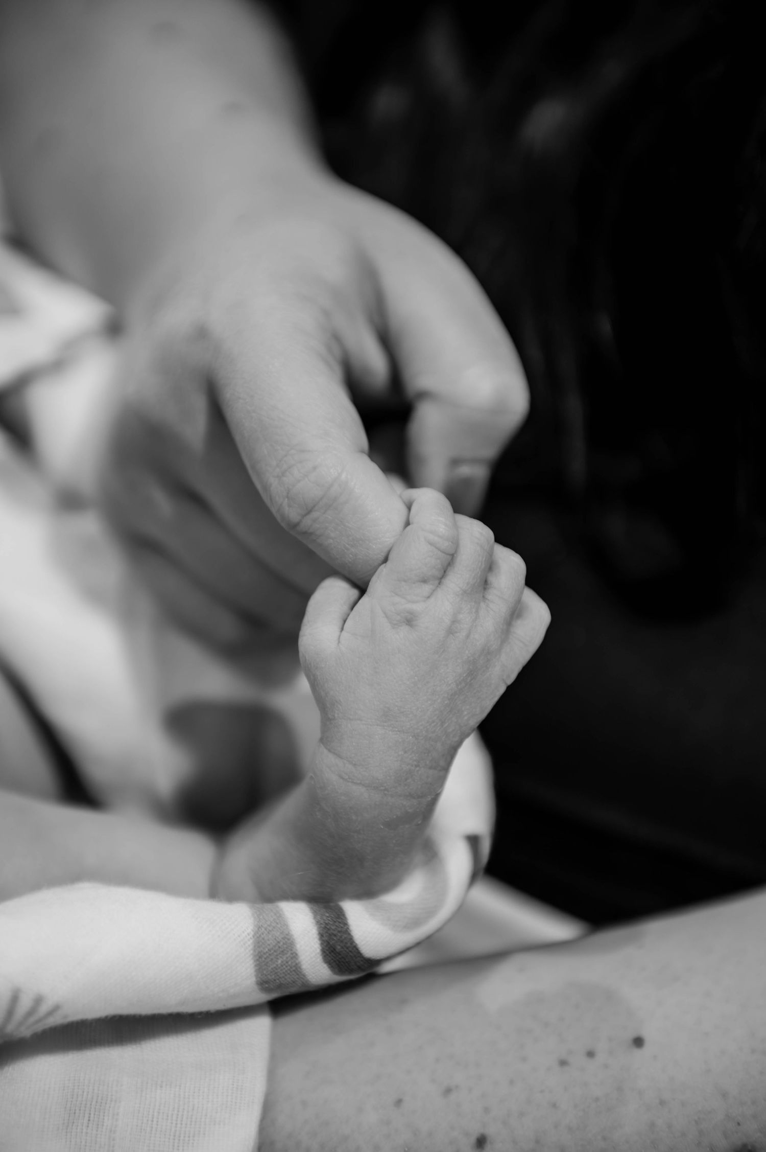 Close-up of a tiny newborn hand grasping an adult finger in an emotional black and white capture.