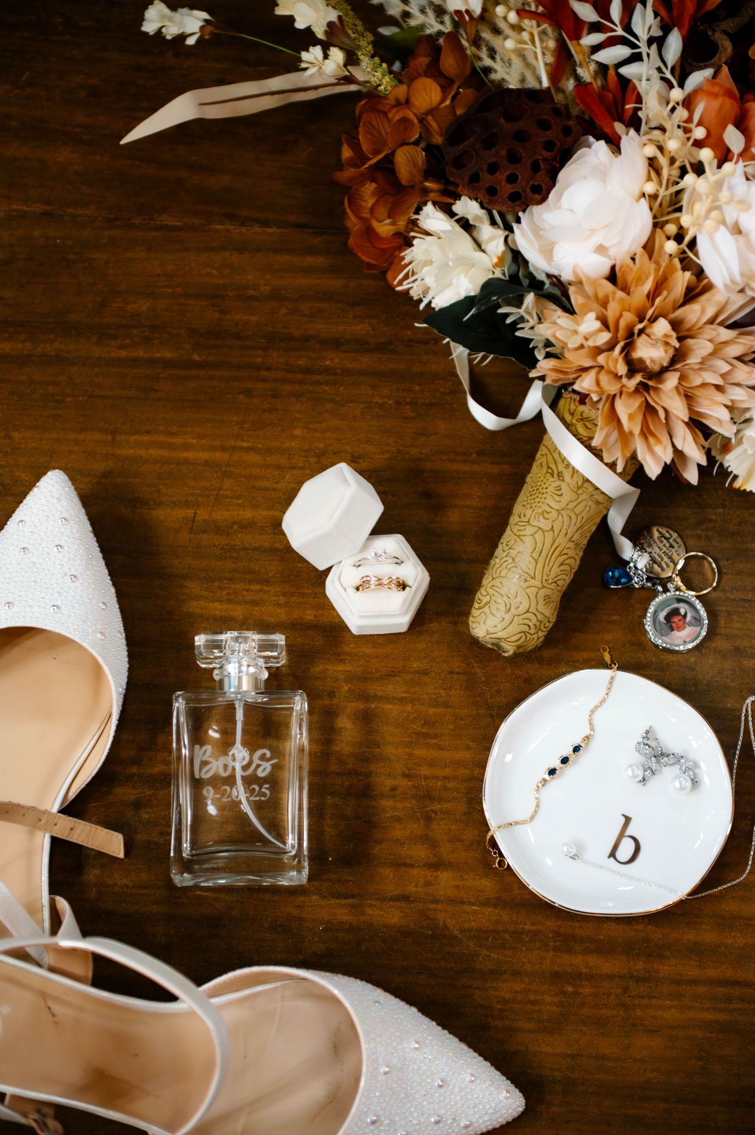 Wedding details including flowers, perfume bottle and accessories arranged on dark wooden surface.