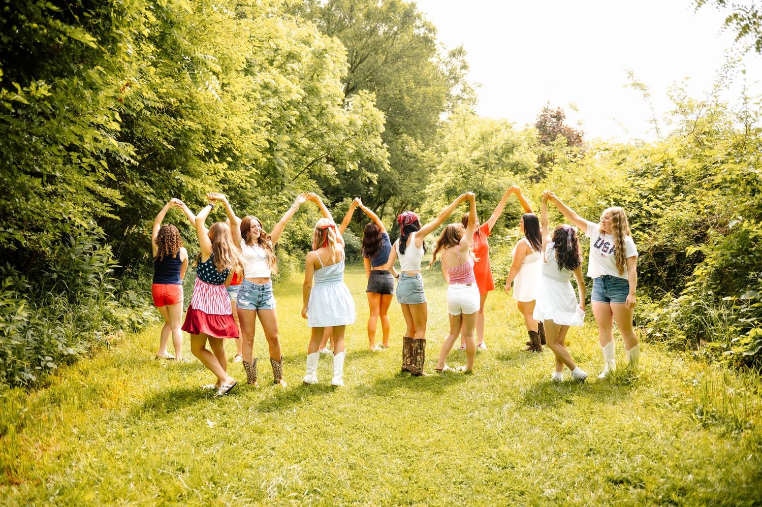 Group of friends running and celebrating together on a grassy path surrounded by trees.