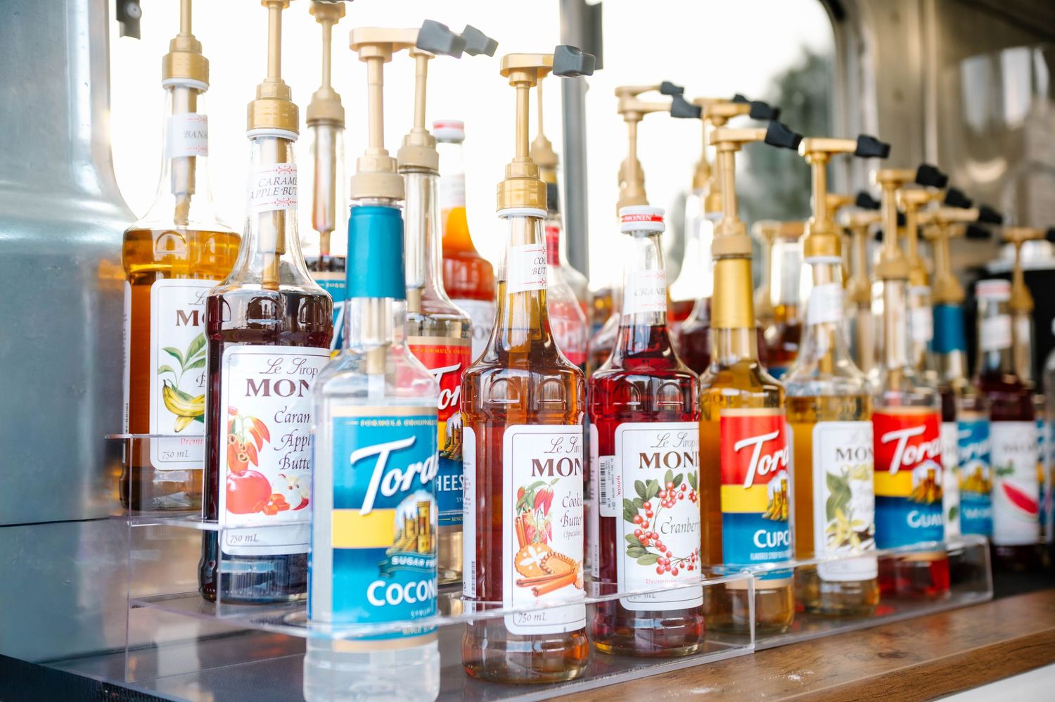 Row of syrup bottles and drink dispensers lined up on a counter.