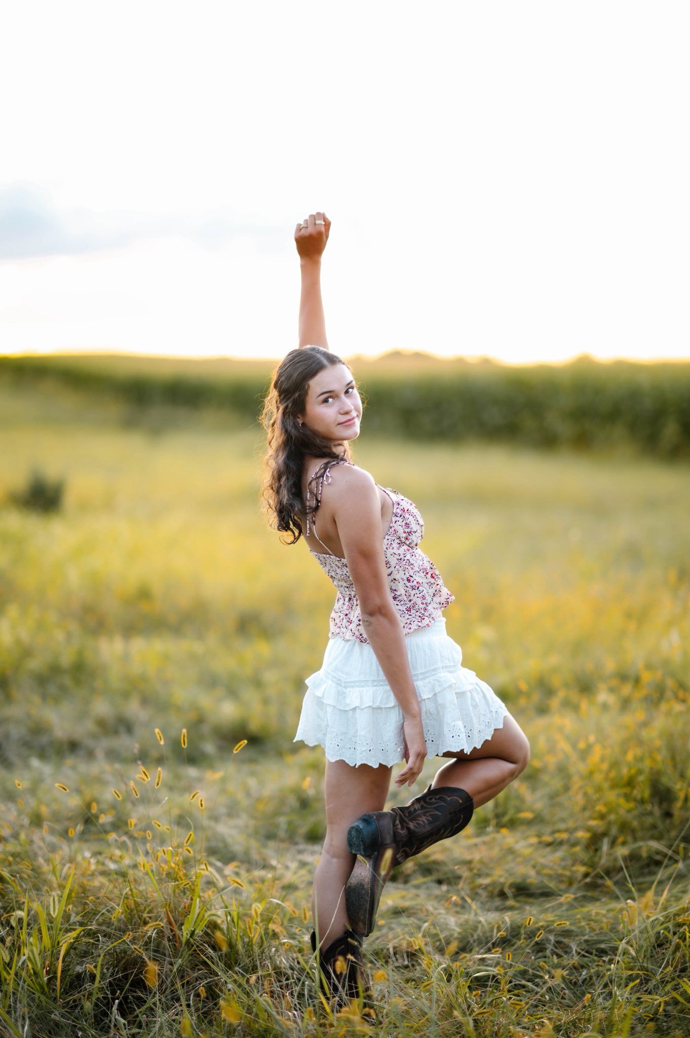 A person in a white dress twirls playfully in a sunlit meadow during golden hour.