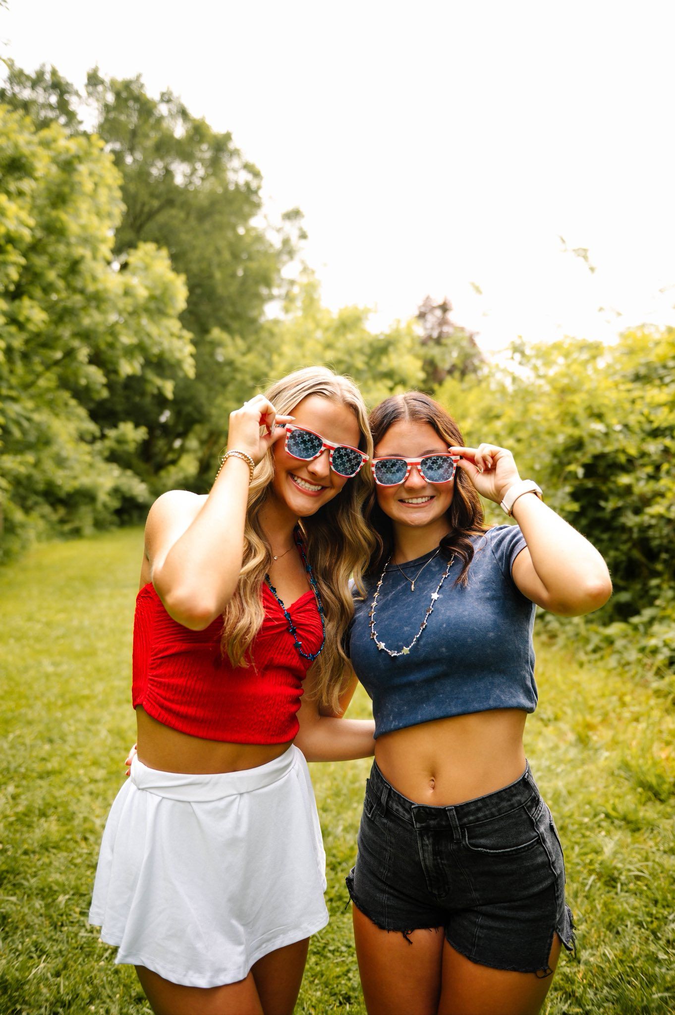 Two friends wearing patriotic sunglasses pose together on a sunny summer day.