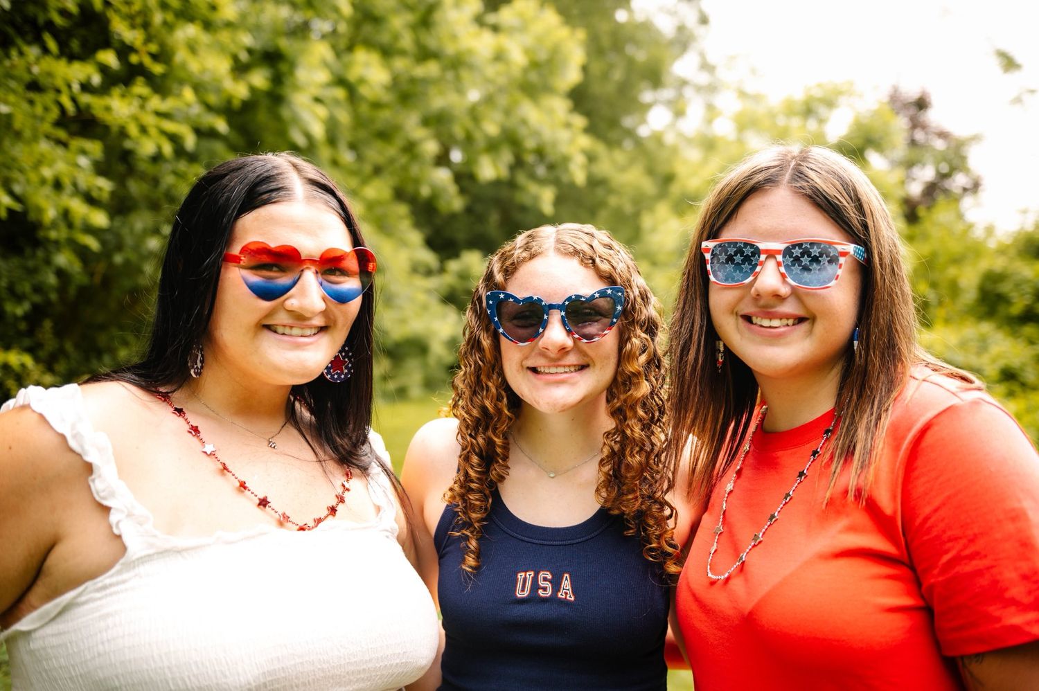 Friends in patriotic outfits and sunglasses pose together outdoors.