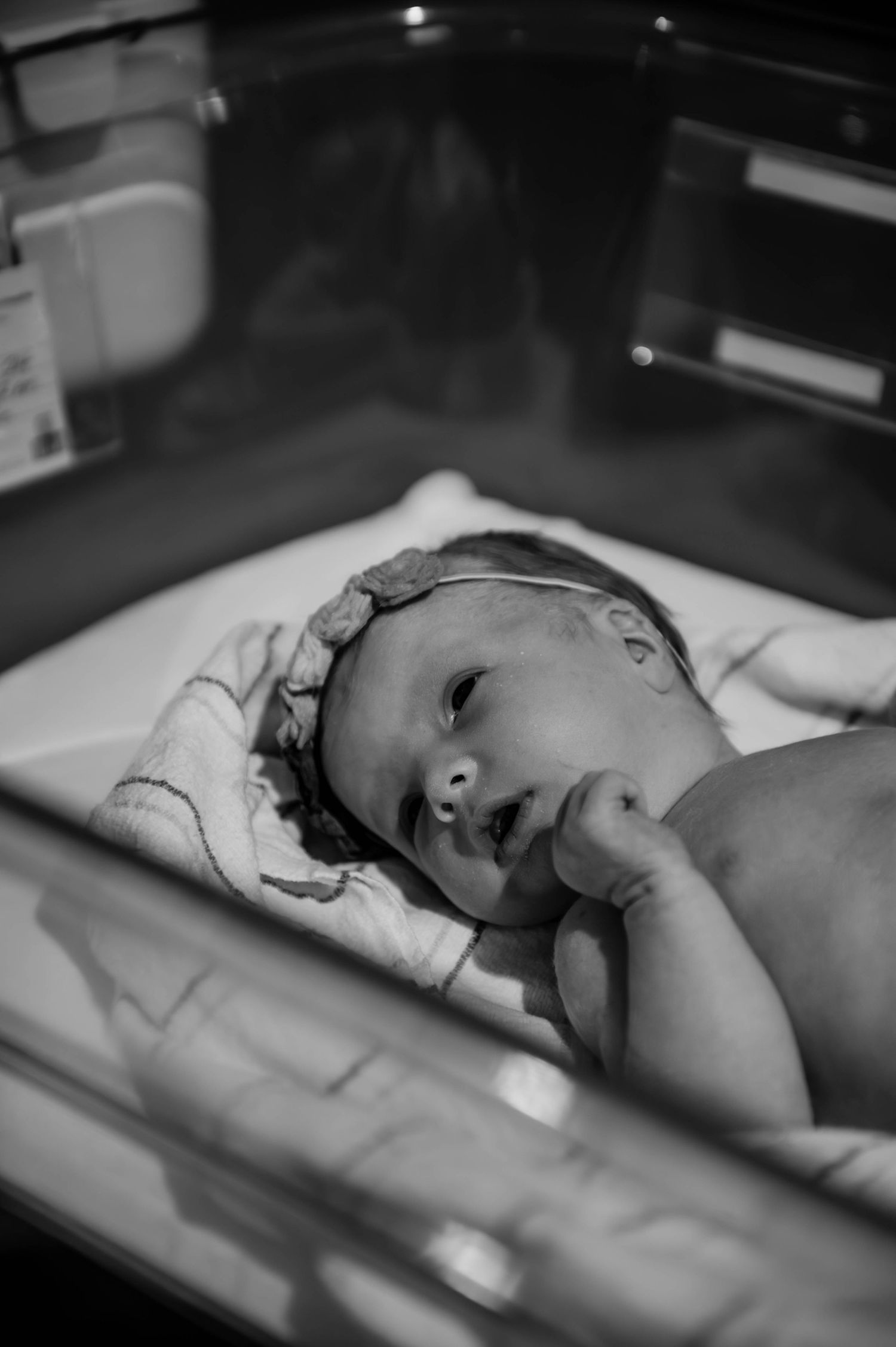 A newborn rests in a hospital bassinet while being monitored with medical equipment.