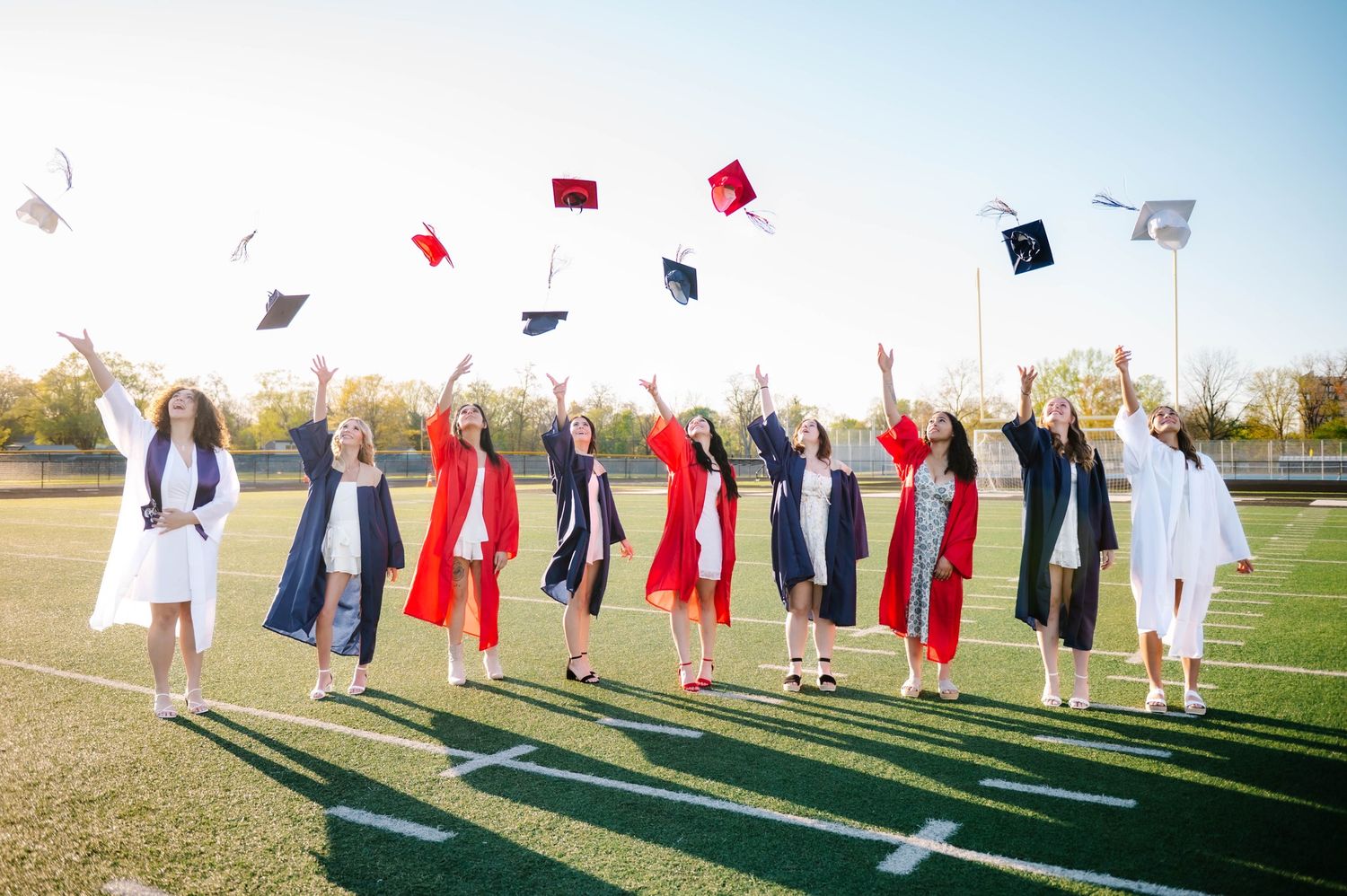 Graduates throwing their caps in the air on a sunny day while wearing red and white gowns.