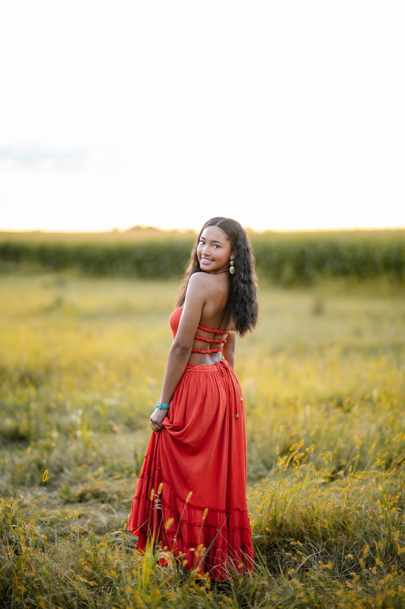 A flowing red dress catches the light during a sunset photoshoot in a meadow.