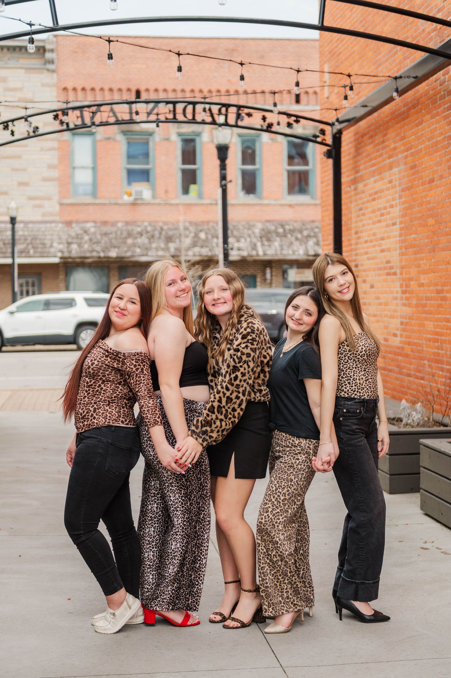 Five young women in coordinating leopard print outfits smile and pose together under string lights.