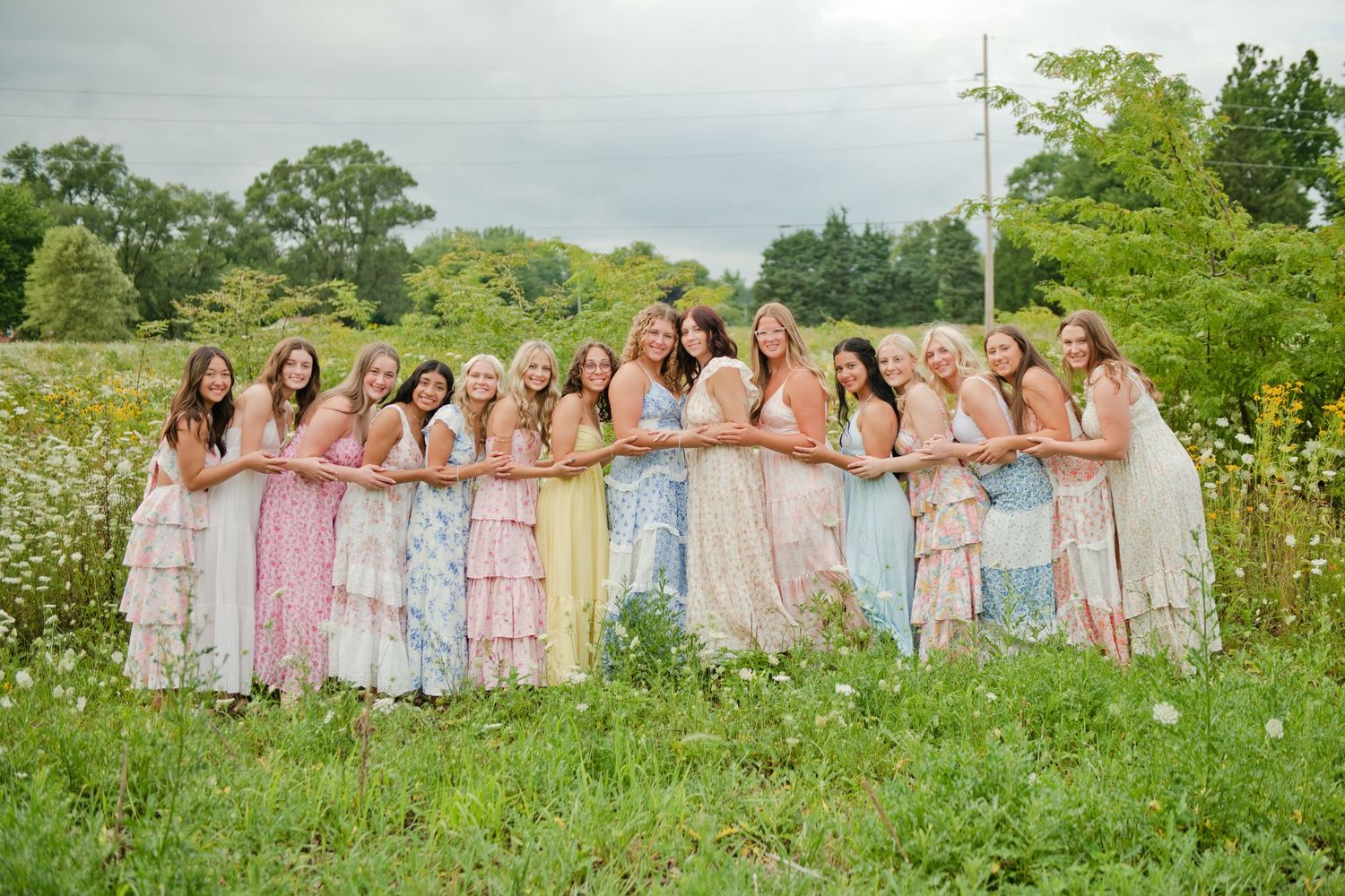 Group of bridesmaids in colorful floral dresses posing in a wildflower meadow.