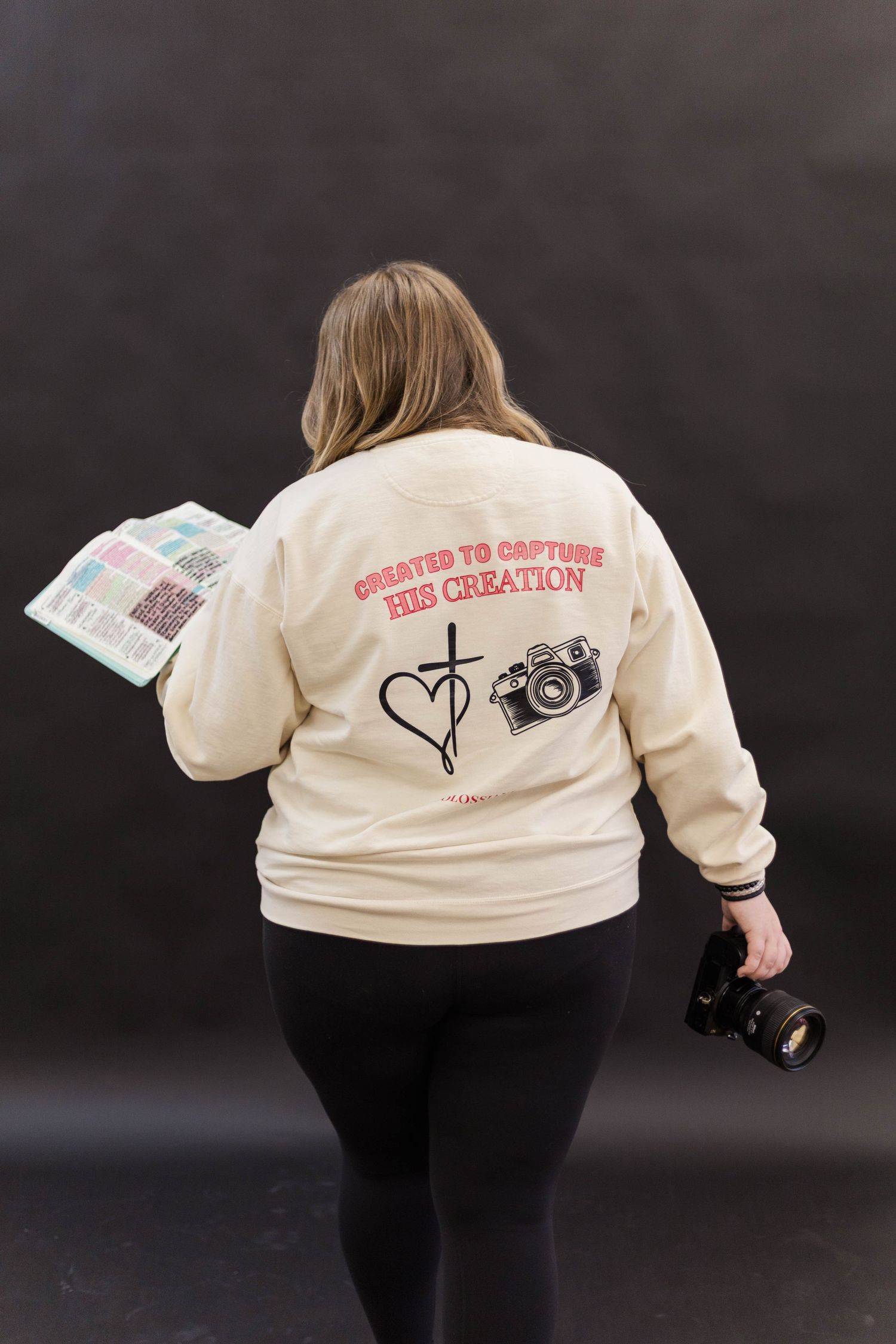 Cream-colored sweatshirt with camera and heart graphics displayed on dark background.