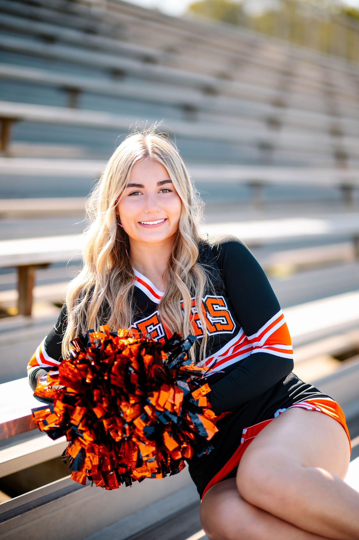 Cheerleader in uniform reclines on stadium bleachers during a sunny photoshoot.