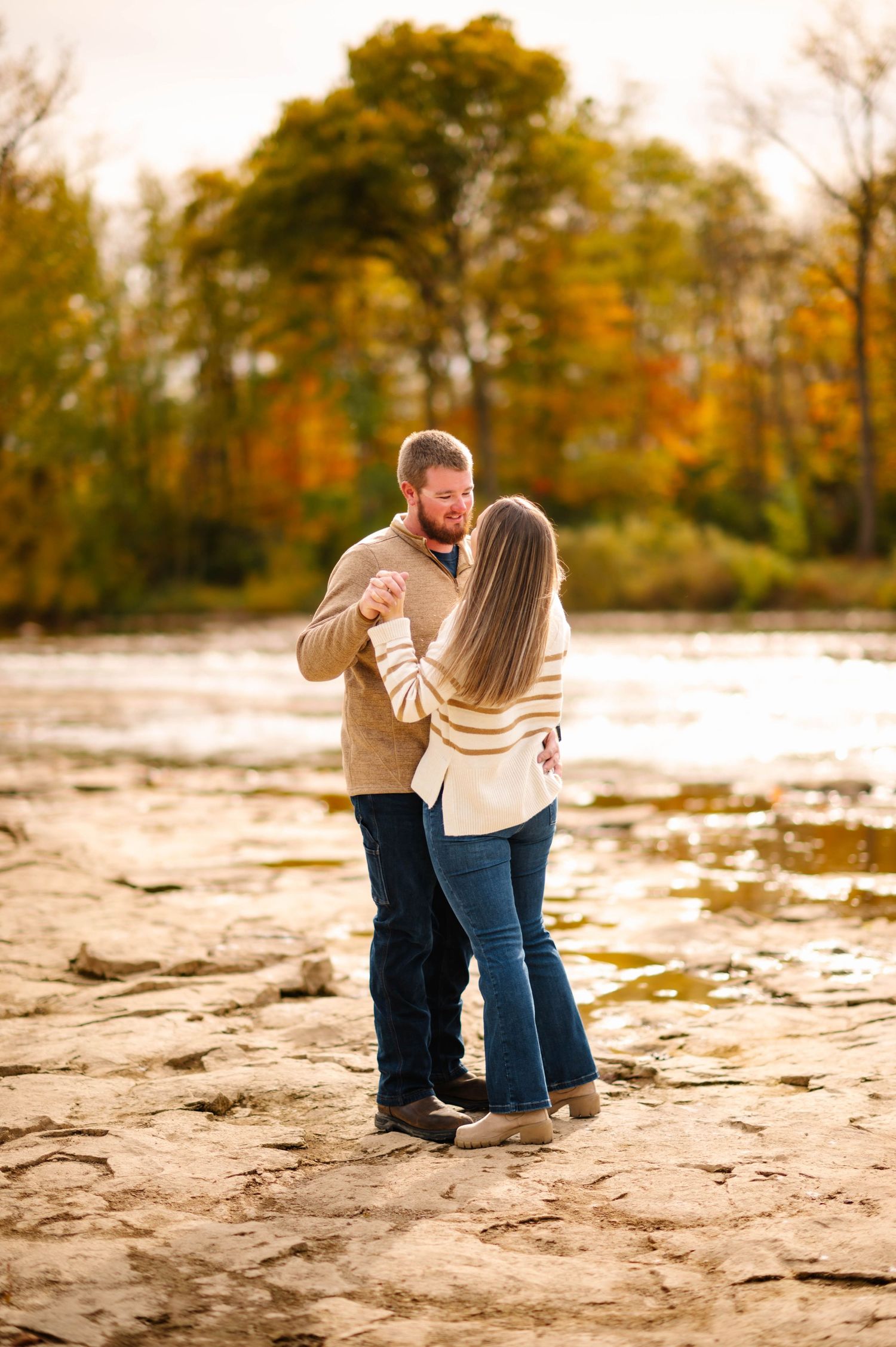 Couple in coordinating outfits pose together on rocky riverbank during golden hour.