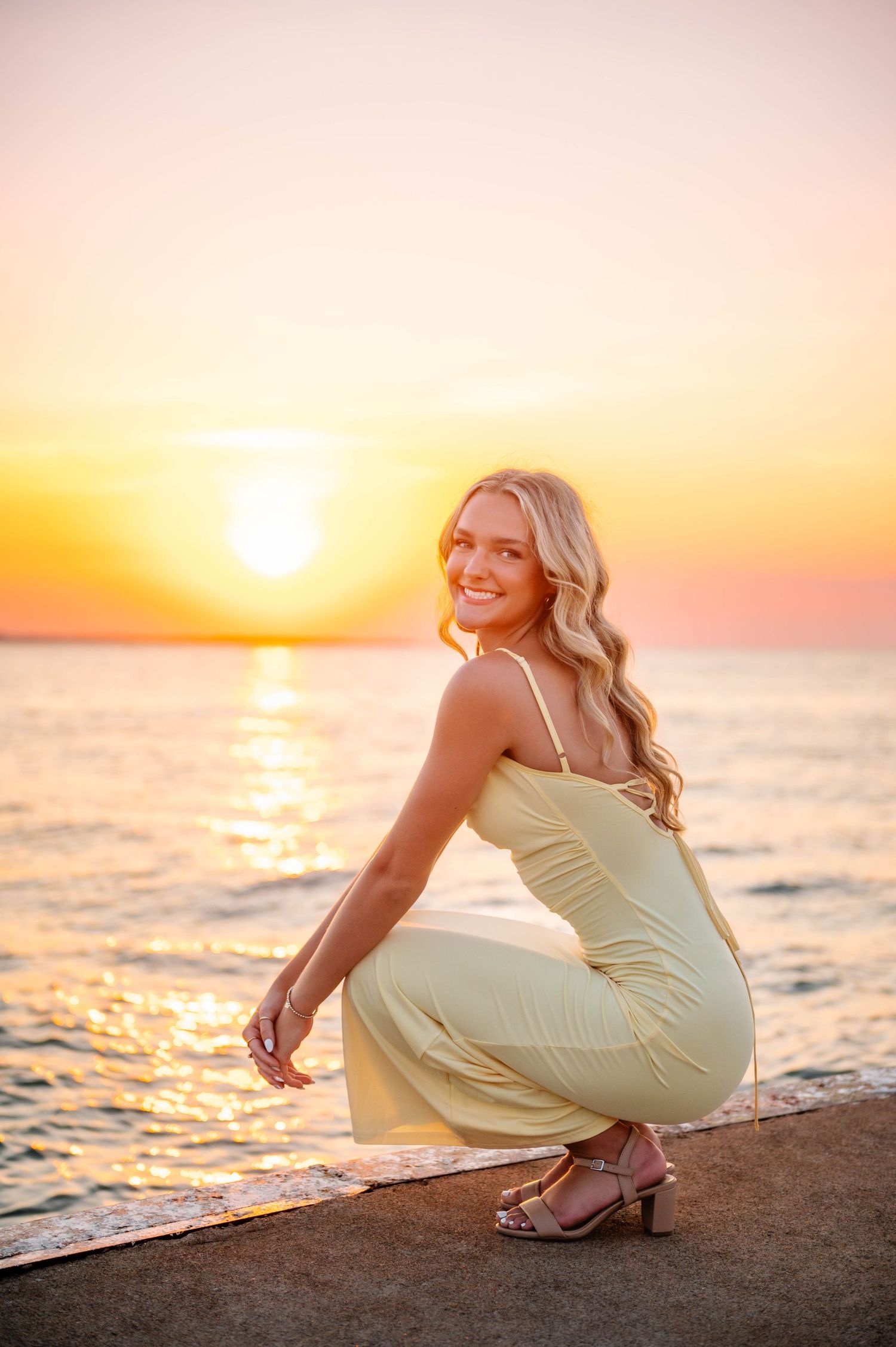 Elegant portrait session at sunset with person in yellow dress sitting by the ocean.