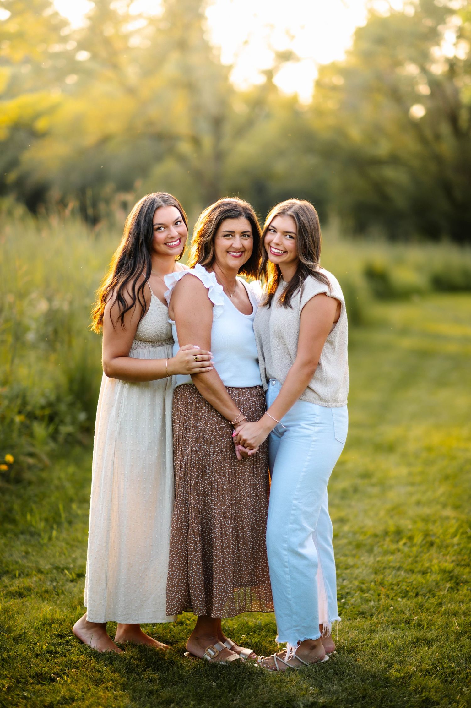 Three people embrace while standing in a sun-drenched field at sunset.