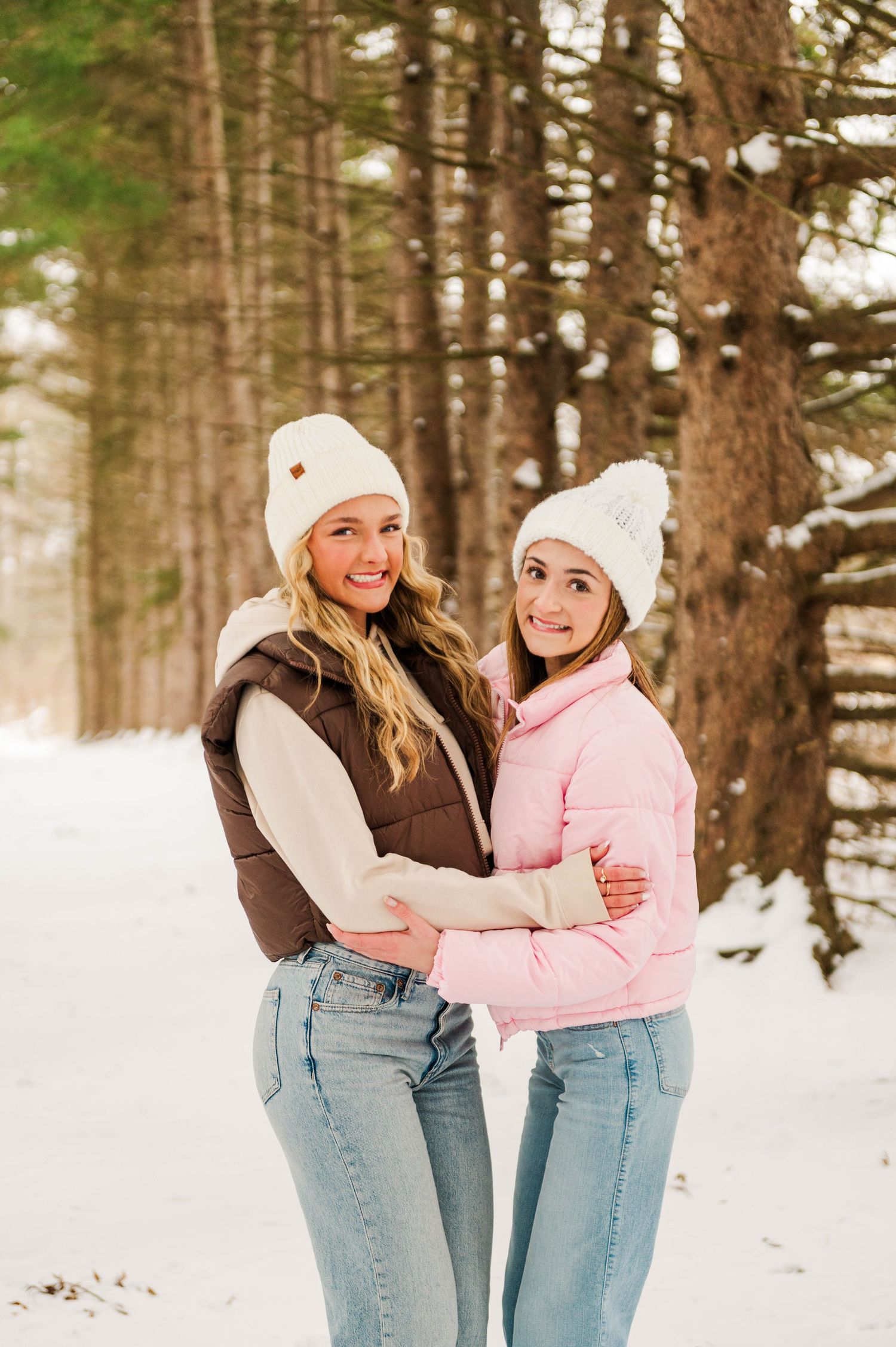 Two people in matching winter outfits sharing a moment in a snowy pine forest.