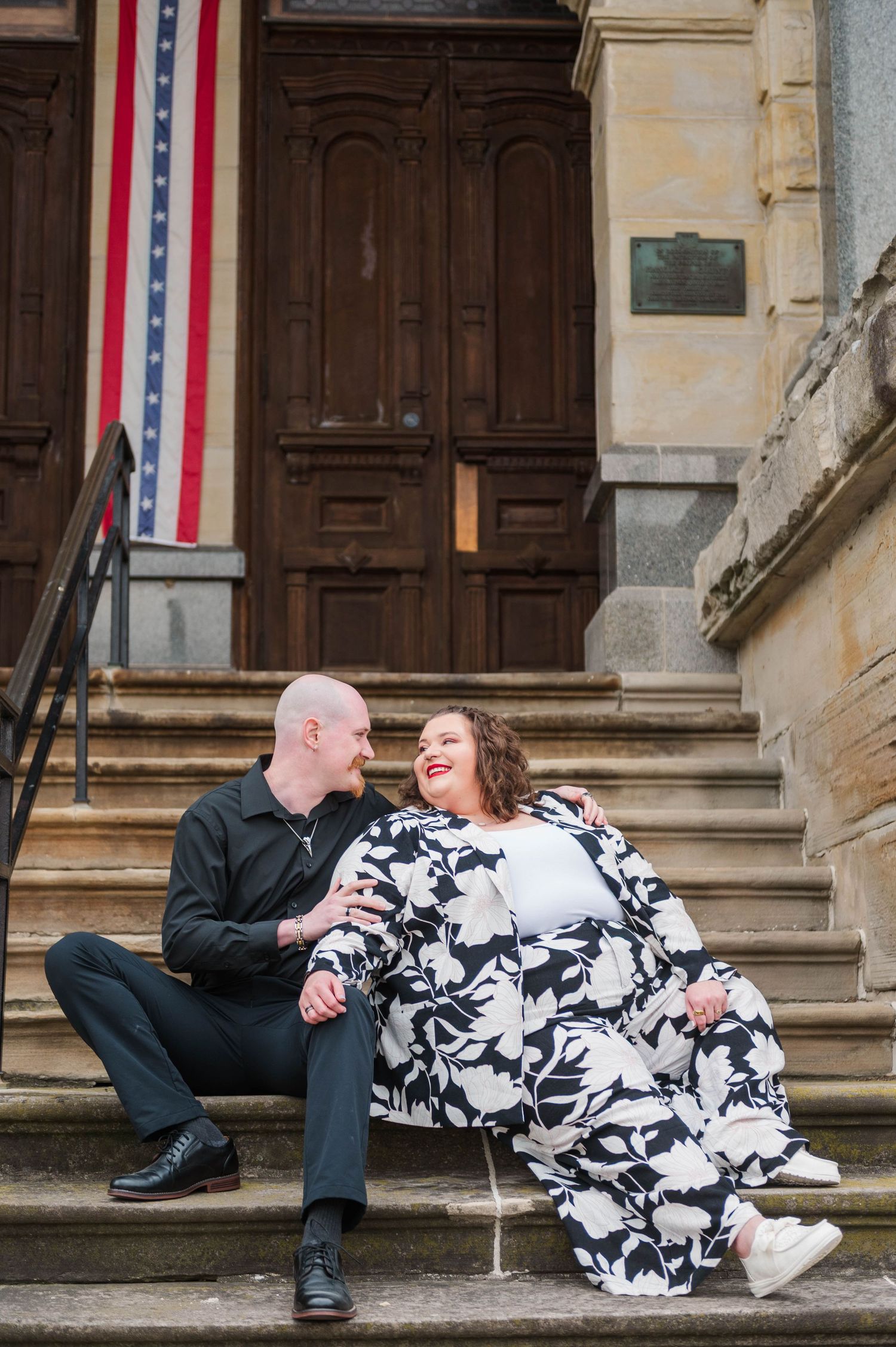 A couple sharing a joyful moment while sitting on stone steps with an American flag banner.