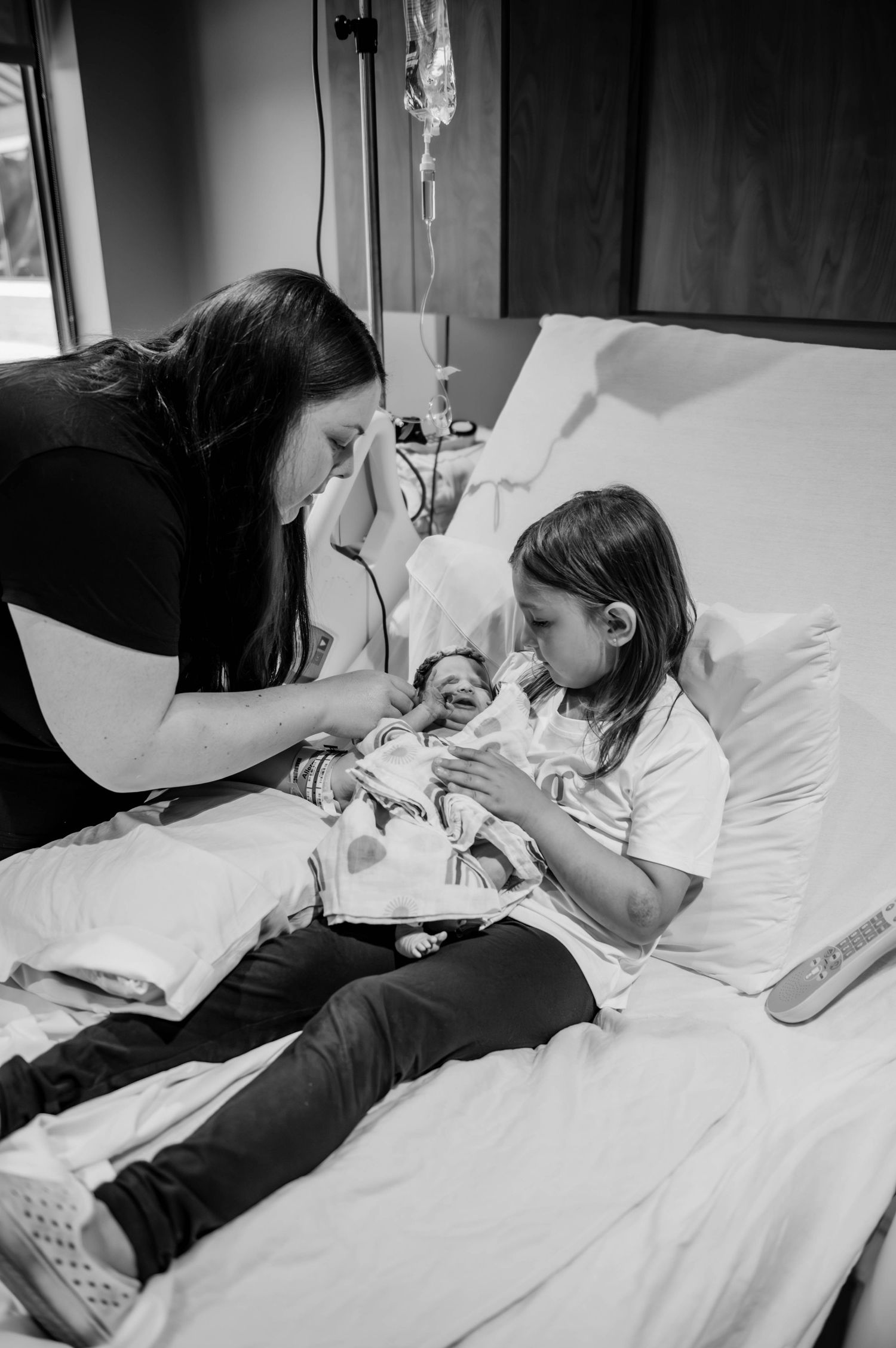 Family members interact with a newborn on a hospital bed in black and white.