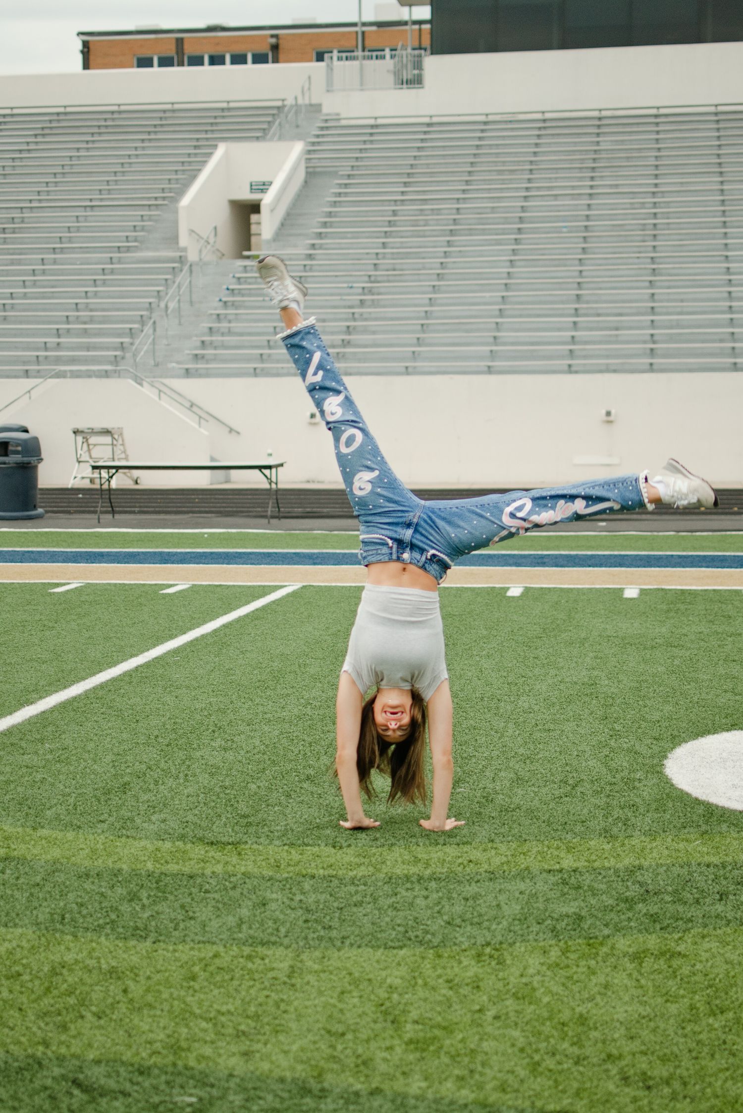 Girl performs a cartwheel in painted senior jeans and white top on a football field.