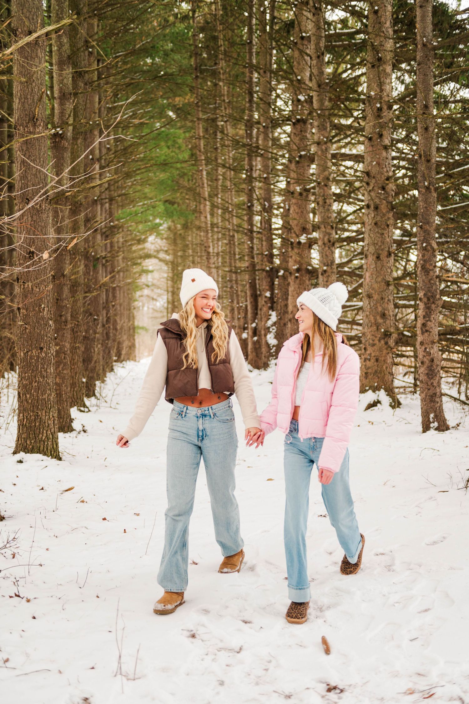 Two friends laugh and dance together on a snowy forest trail.