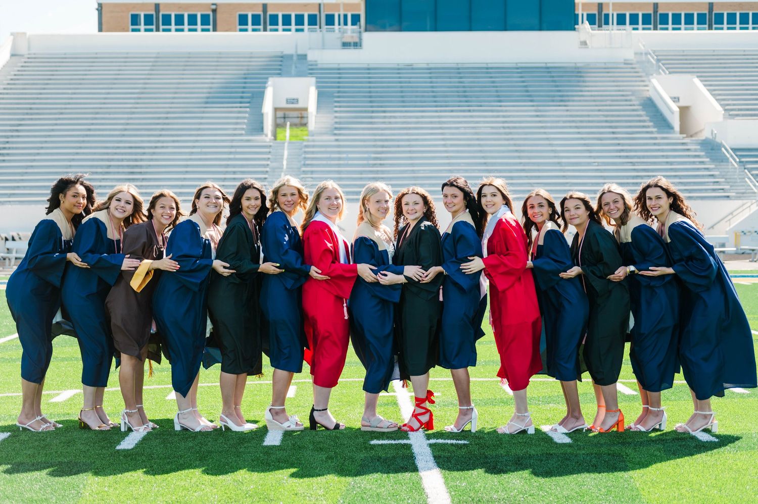 Group of women in navy and red graduation gowns posing on a football field stadium, celebrating their graduation.