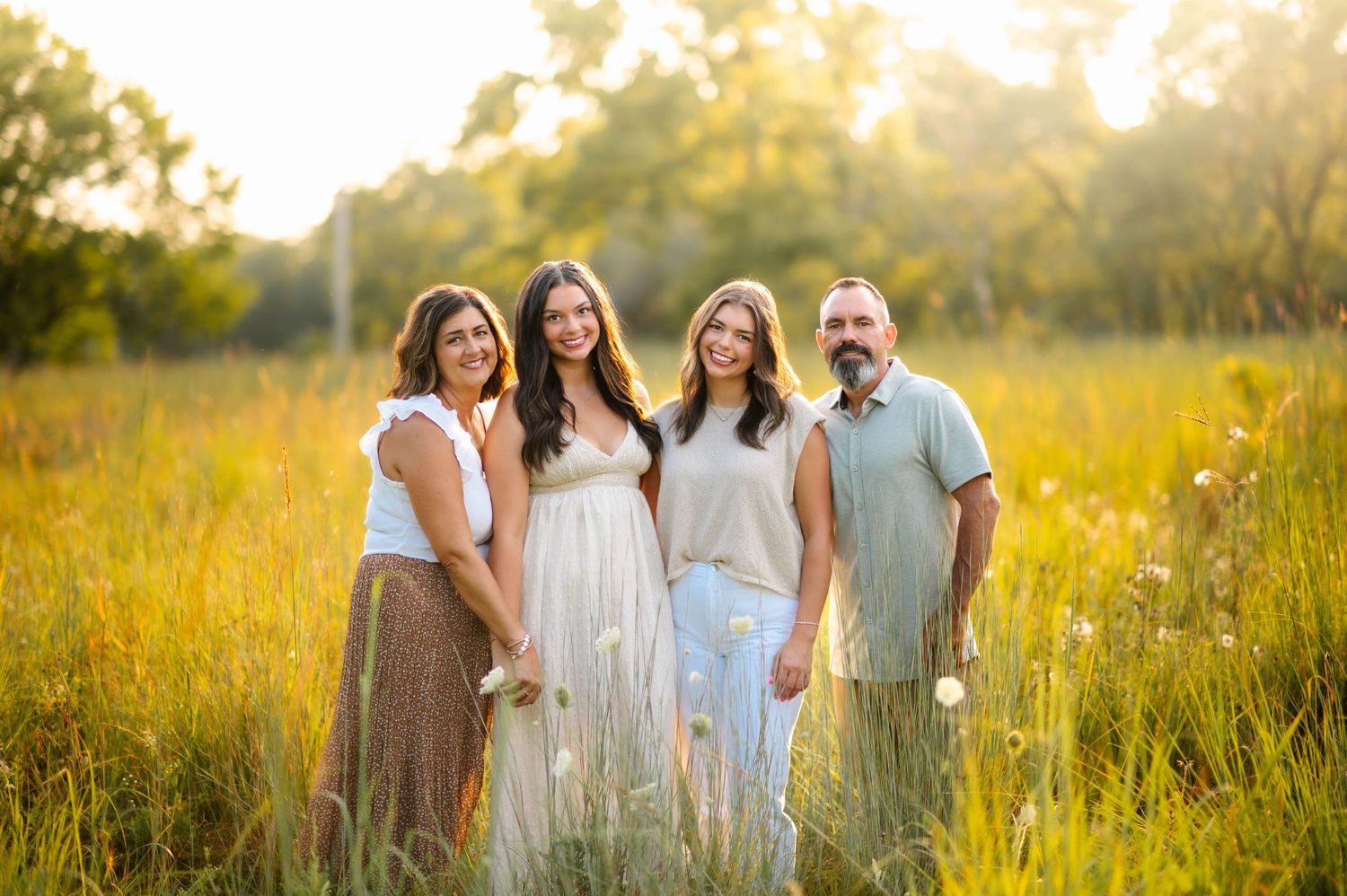 A group poses together in tall grass with golden sunlight filtering through trees behind them.